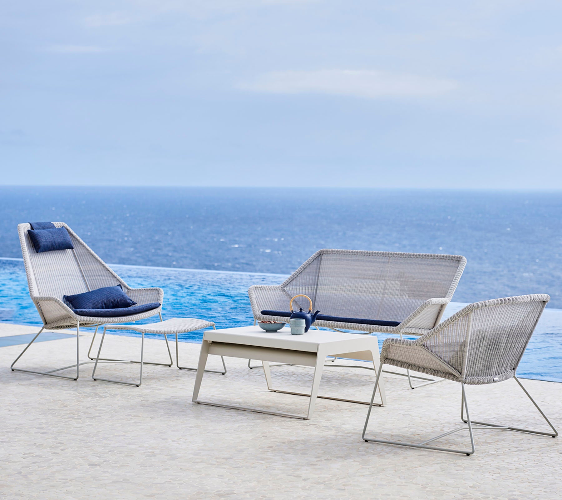 Conjunto de muebles de exterior moderno que incluye sillas elegantes y una mesa, con un fondo de agua y cielo.
