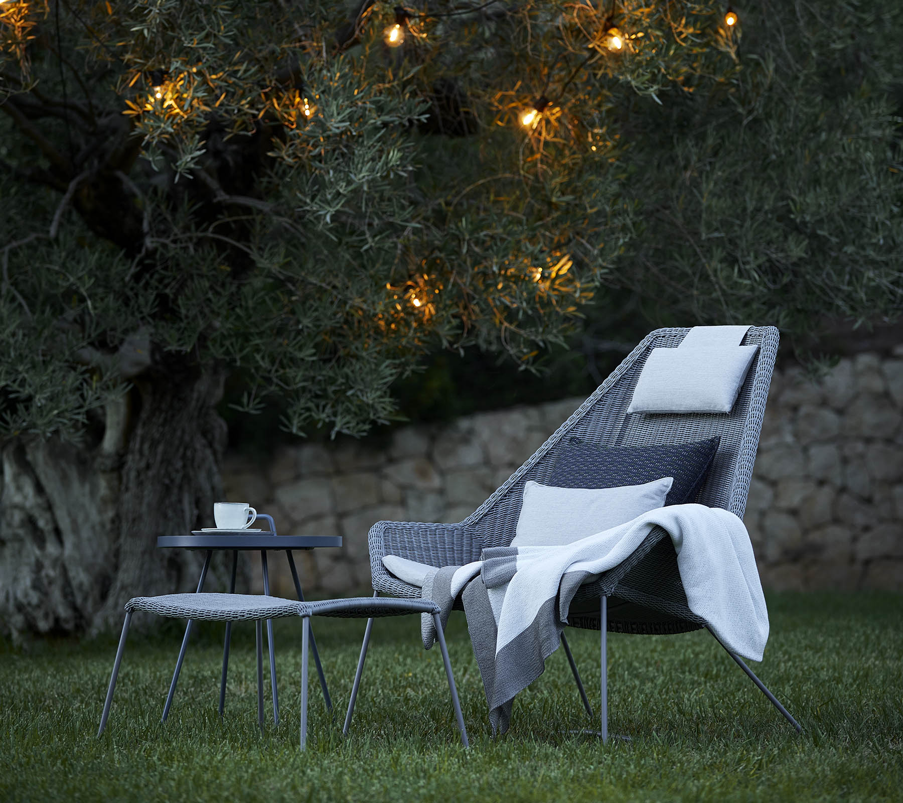 Arreglo de asientos elegante con una silla acogedora, una manta suave y una mesa auxiliar, iluminado por luces suaves en el fondo.