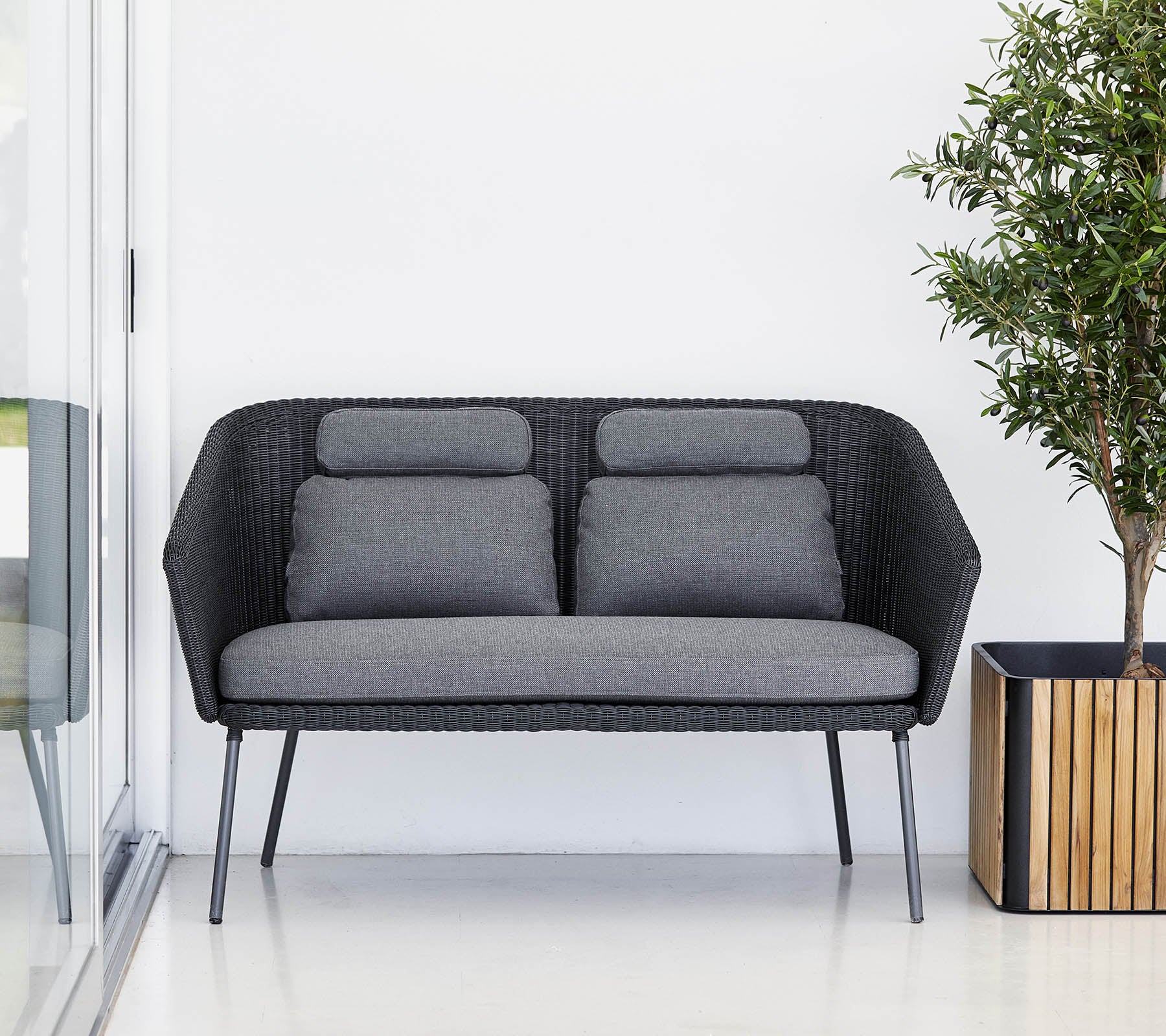 Sofá negro elegante con cojines grises, complementado con una planta en maceta en una maceta de madera. Diseño moderno y minimalista.
