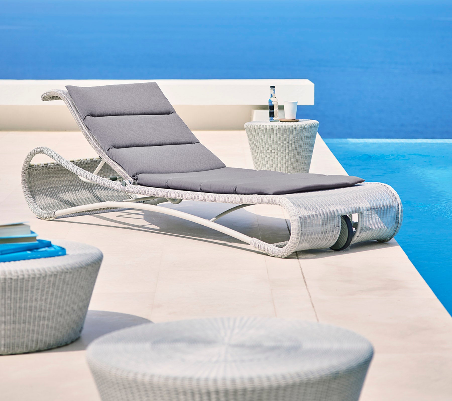 Sillón elegante con cojín gris junto a mesas auxiliares modernas, contra un fondo azul sereno. Perfecto para relajarse.