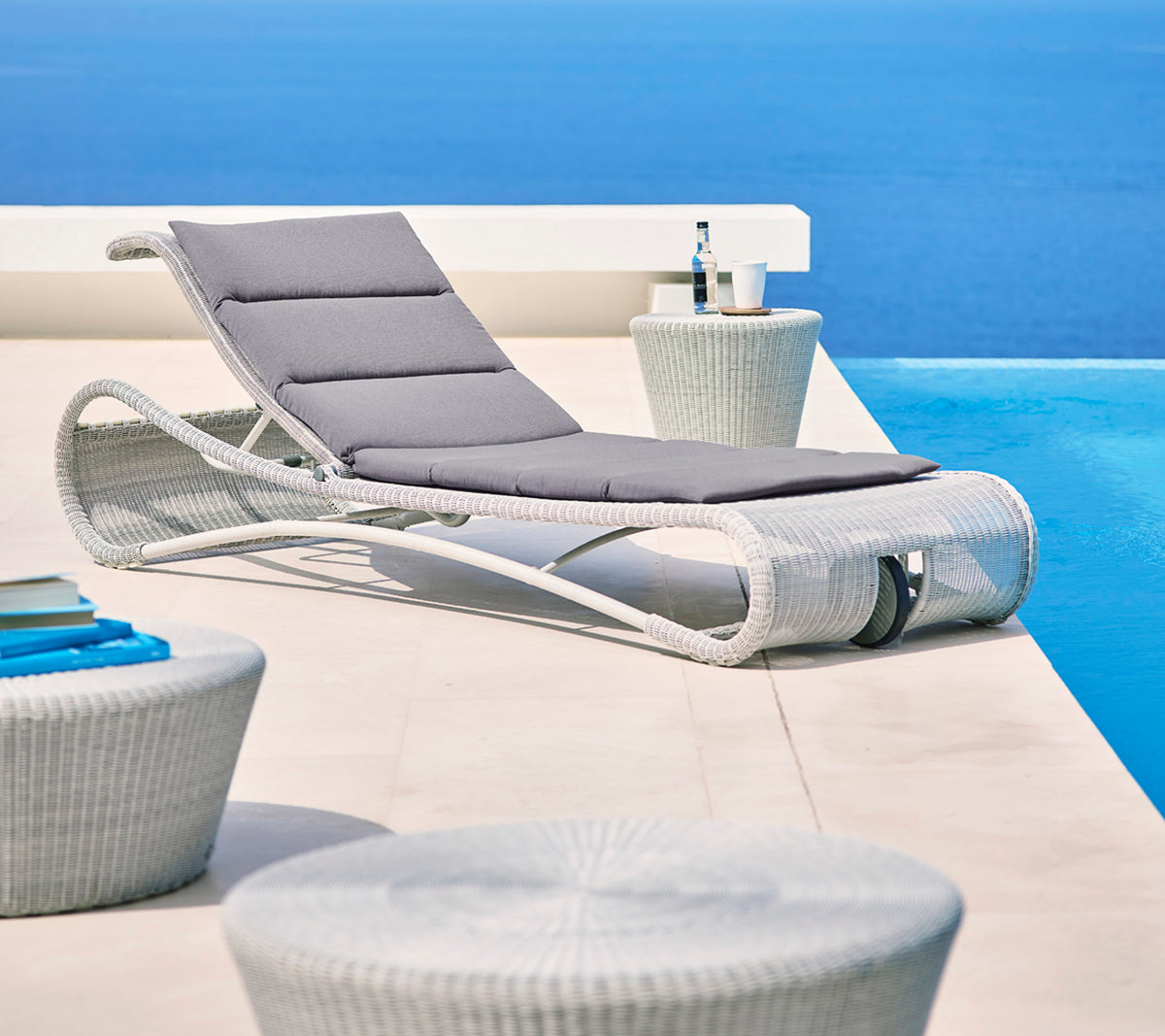 Sillón elegante con cojín gris junto a mesas auxiliares modernas, contra un fondo azul sereno. Perfecto para relajarse.