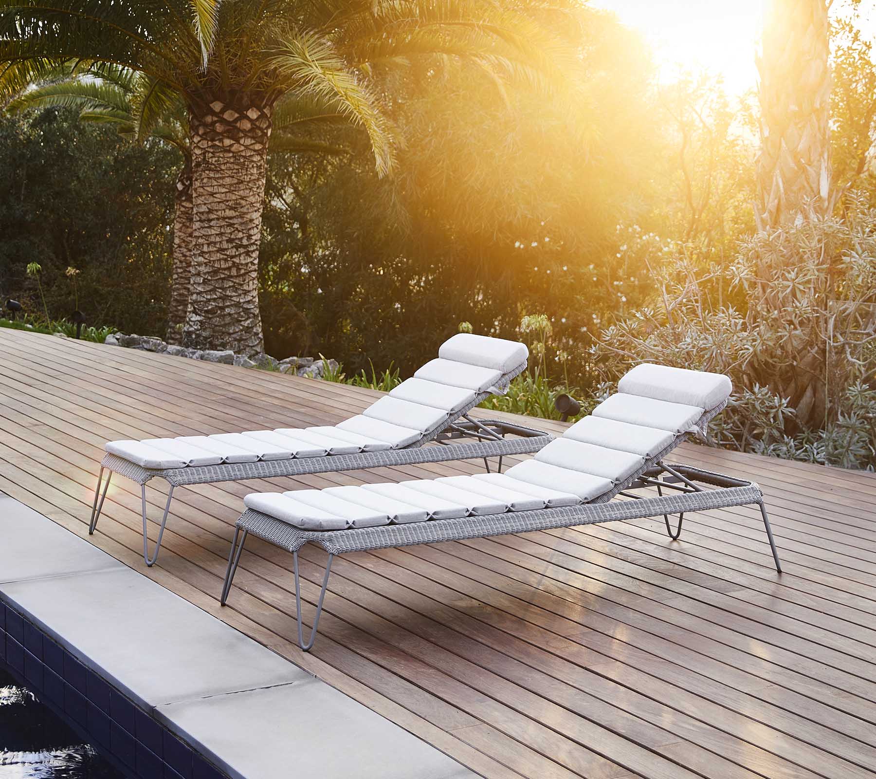 Dos sillas de salón elegantes con cojines blancos, situadas junto a una piscina y rodeadas de exuberante vegetación, disfrutando de la cálida luz del sol.