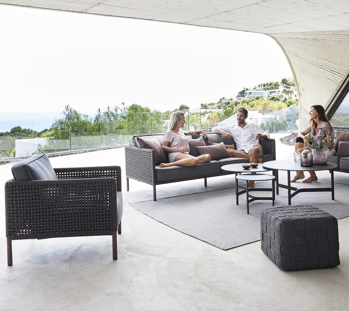 Una acogedora zona de estar con una mesa de café, sillas elegantes y personas disfrutando de una conversación relajada con un fondo escénico.
