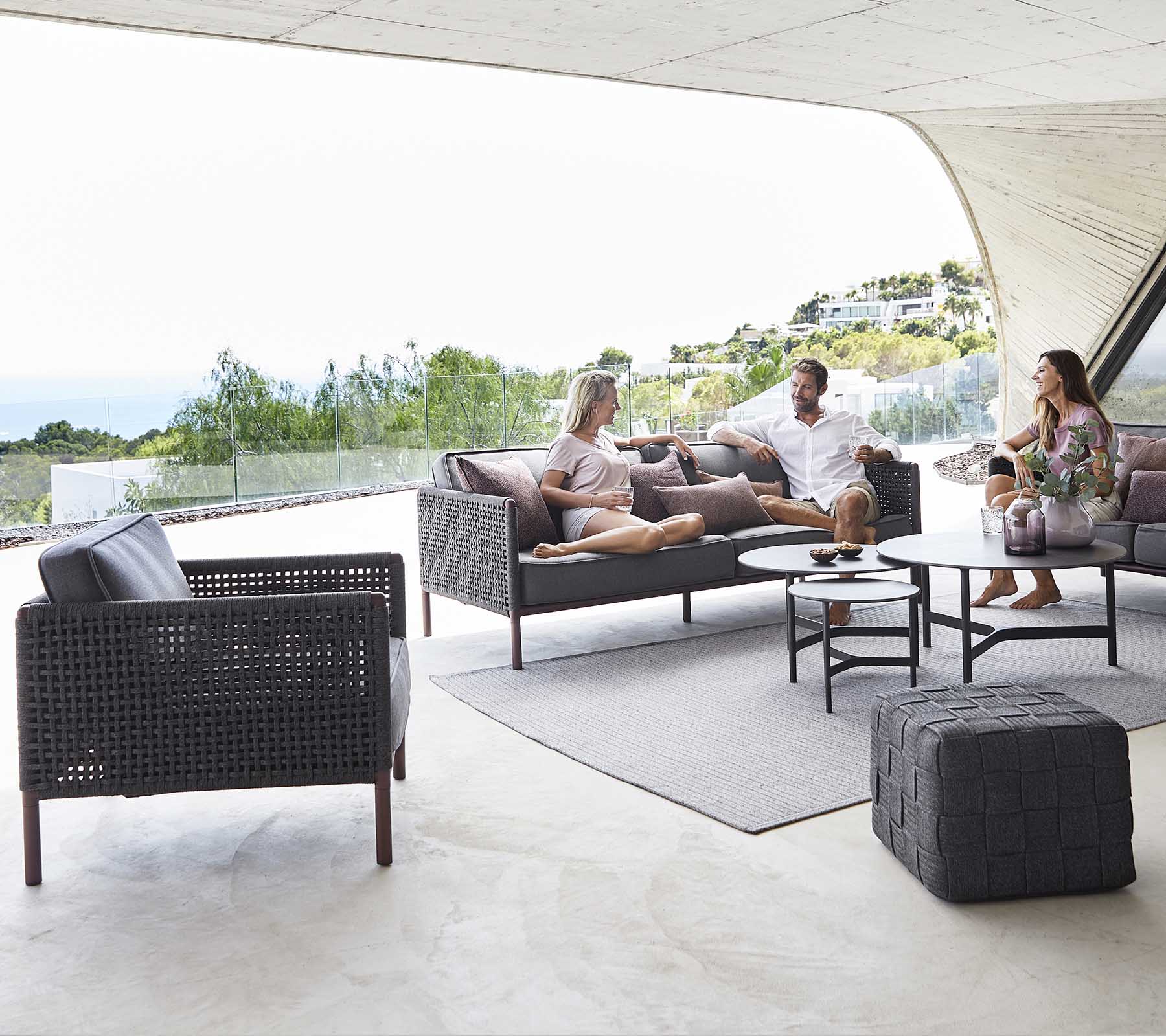 Una acogedora zona de estar con una mesa de café, sillas elegantes y personas disfrutando de una conversación relajada con un fondo escénico.