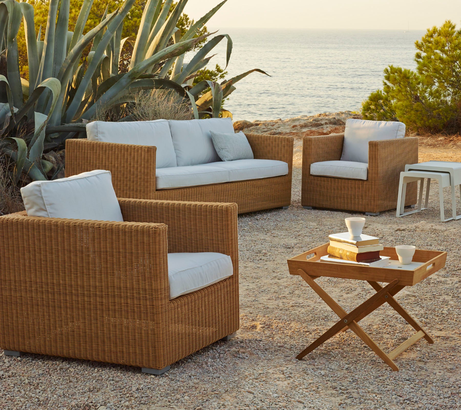 Elegante disposición de asientos al aire libre con sillas de ratán trenzado y un sofá con cojines claros, complementada con una mesa de café de madera.