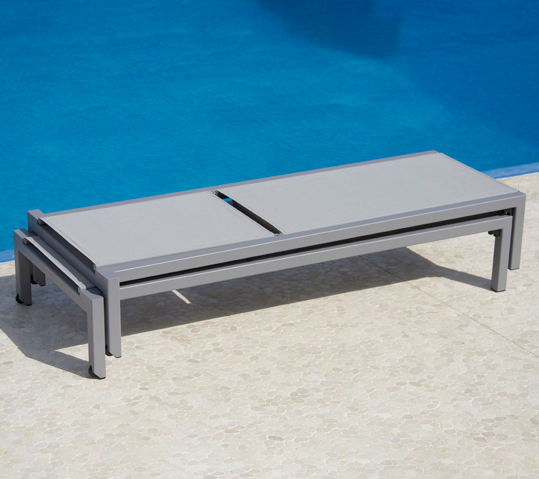 Cama lounge gris elegante al lado de una piscina, con un diseño elegante y funcionalidad práctica para la relajación.