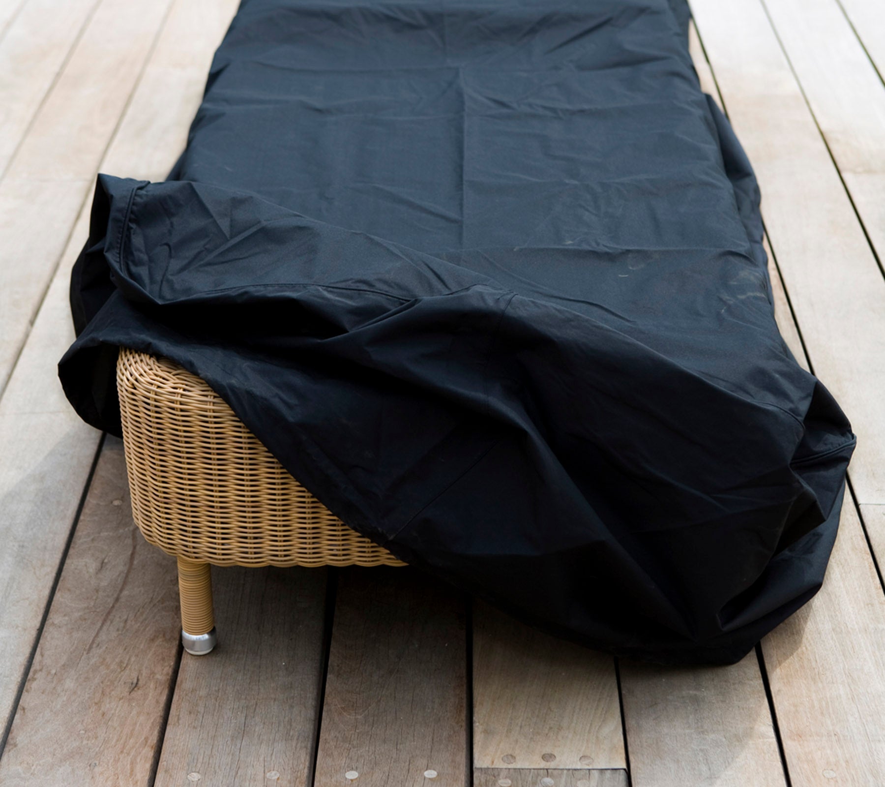 Una pieza de mobiliario de mimbre cubierta con una funda protectora negra, colocada sobre una superficie de madera.
