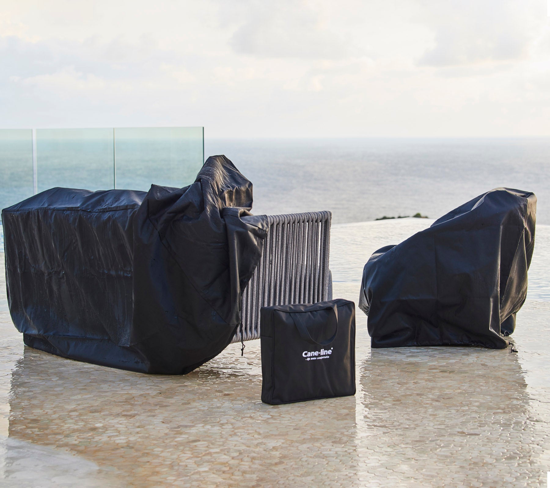 Fundas para muebles de exterior en negro, protegiendo varias piezas de las inclemencias del tiempo, con una funda ordenadamente plegada cerca.