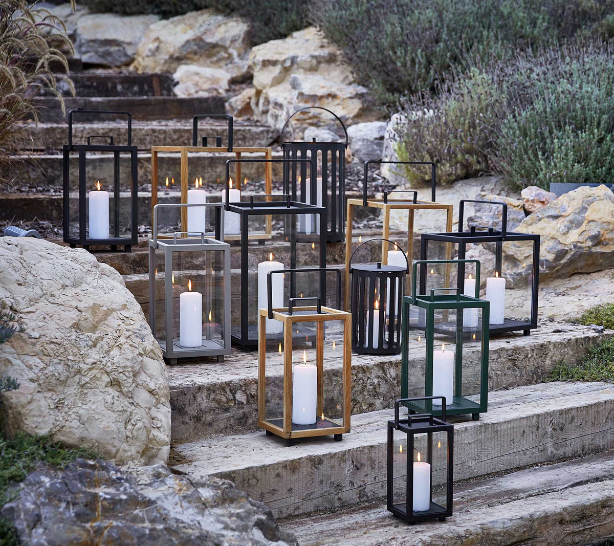 Colección de faroles decorativos en varios estilos y colores, con suave luz de vela, dispuestos artísticamente en escalones de piedra.