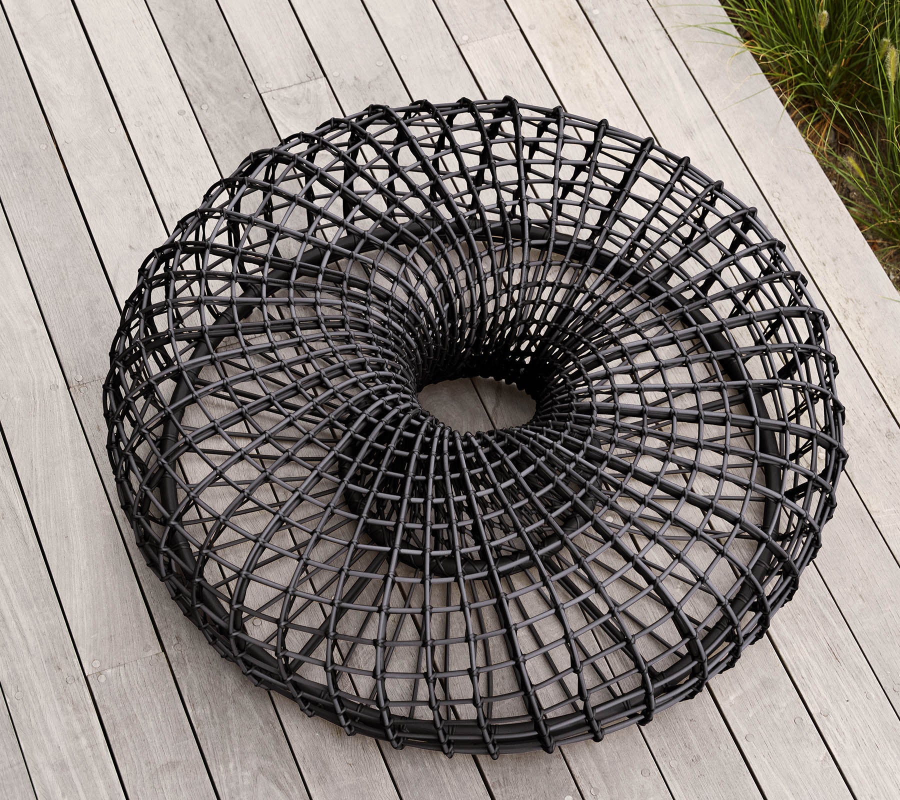 Cesta de alambre negra moderna y circular con un diseño de tejido abierto único, que descansa sobre una superficie plana. Ideal para almacenamiento o propósitos decorativos.