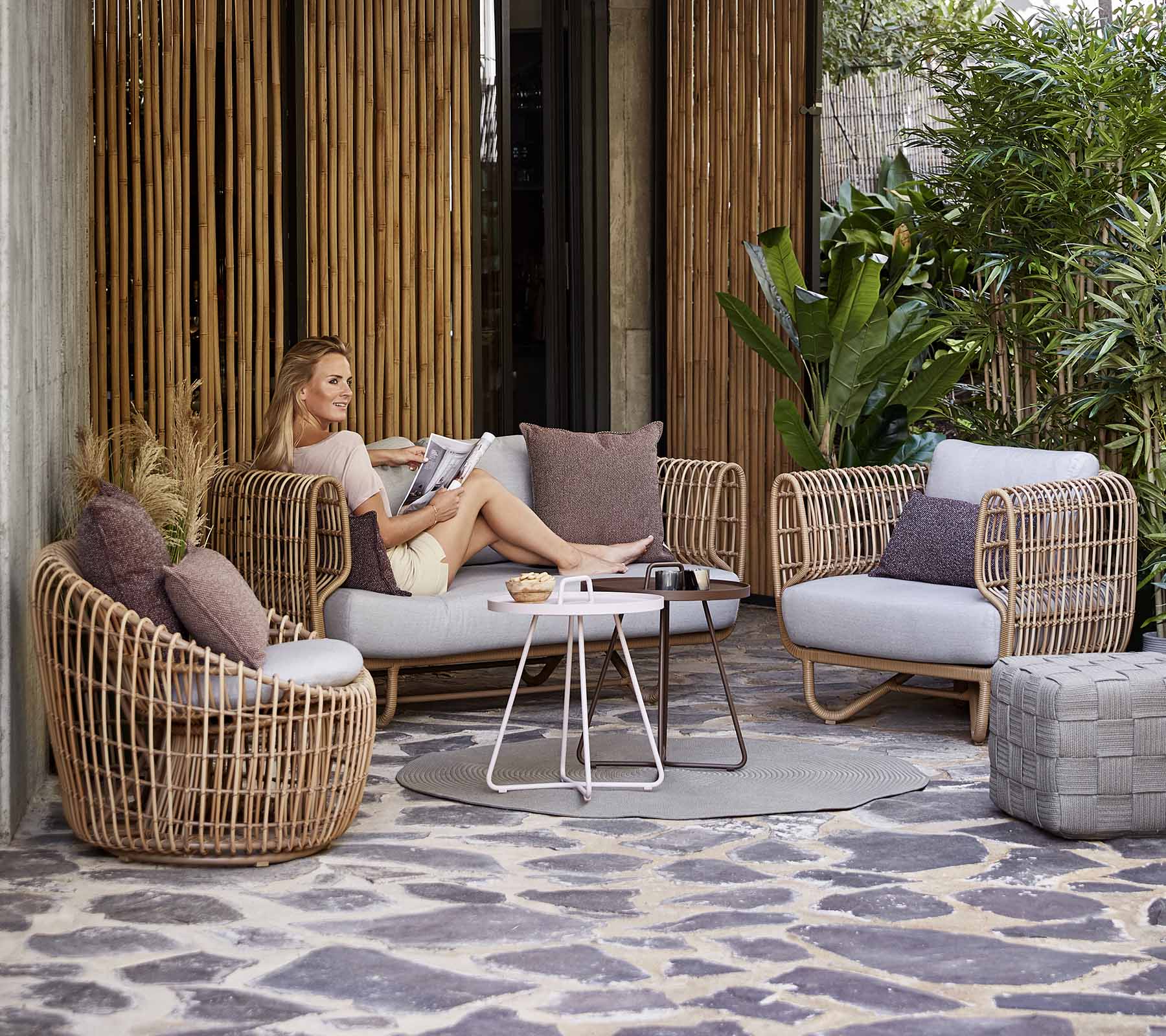 Un arreglo de asientos elegante con muebles tejidos, cojines y una mesa de café, situado entre la vegetación y elementos decorativos.