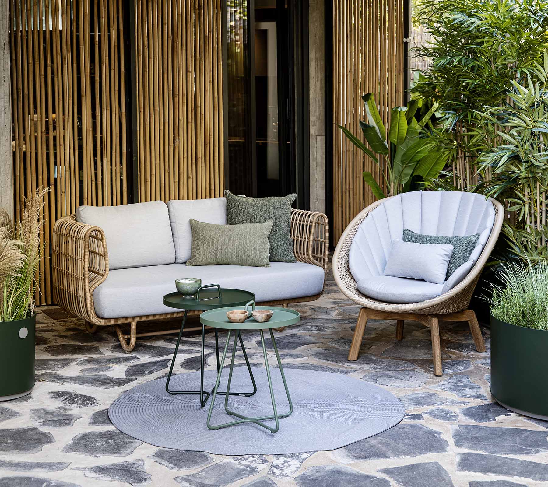 Un acogedor arreglo de asientos con un sofá de mimbre y una silla elegante, acompañado de una mesa pequeña y plantas decorativas.