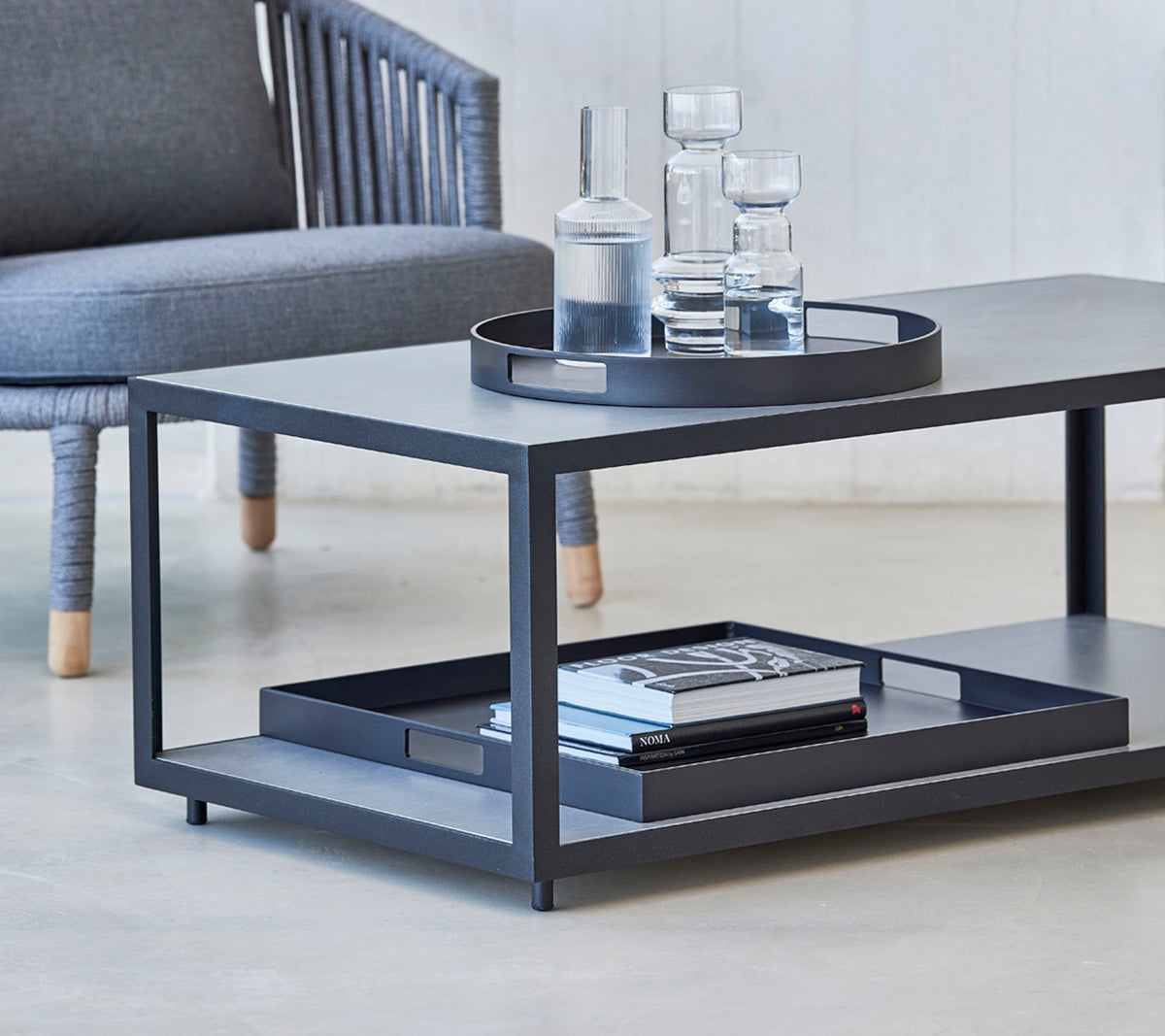 Mesa de café moderna con un diseño elegante, con una bandeja, vasos y libros en la estantería inferior. Ideal para espacios de vida con estilo.
