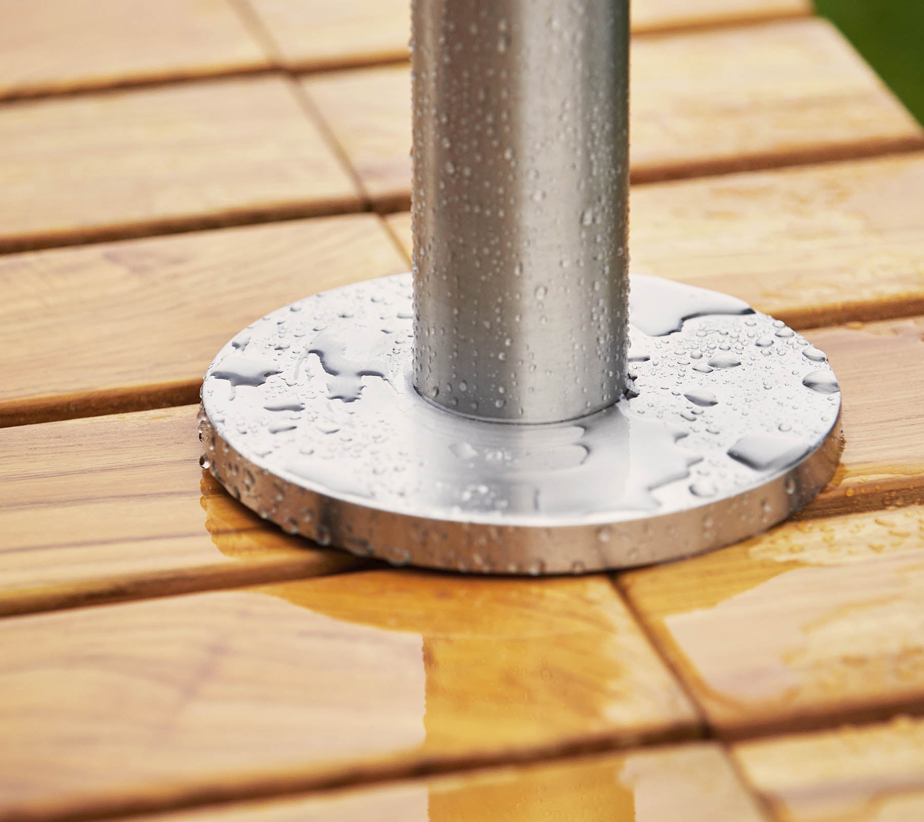 Base de metal con un poste apoyado en una superficie de madera, con gotas de agua tanto en la base como en la madera.