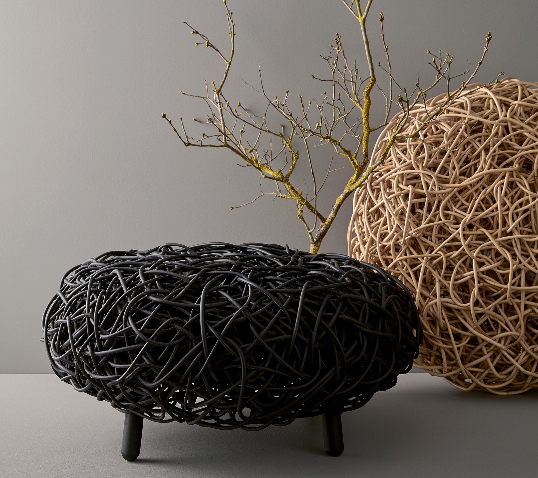 Una mesa de café redonda y elegante hecha de material tejido, que muestra tonos negros y naturales, con una rama decorativa colocada en la parte superior.
