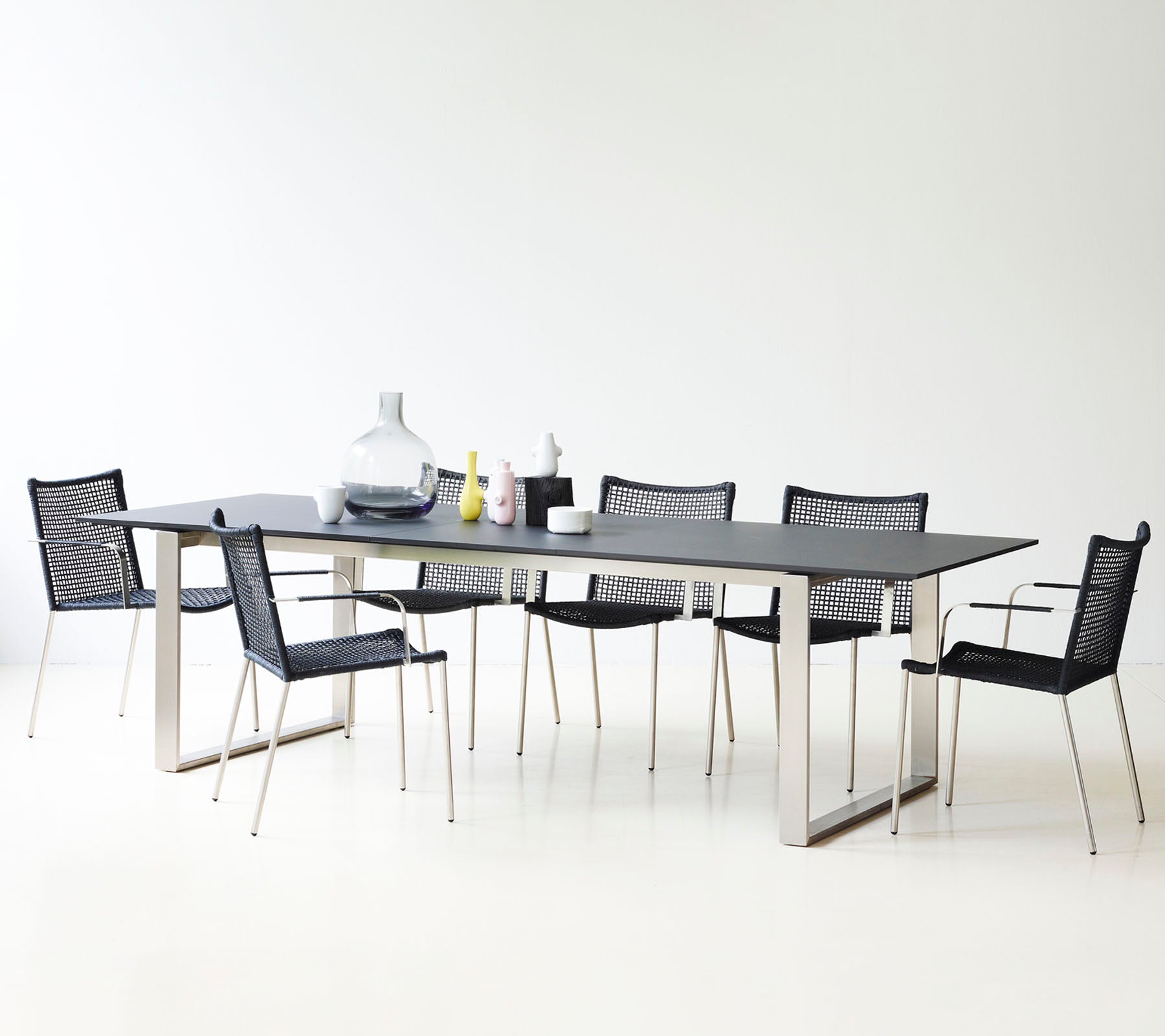 Una mesa de comedor moderna con un diseño elegante, rodeada de sillas de malla negra estilizadas y jarrones decorativos.