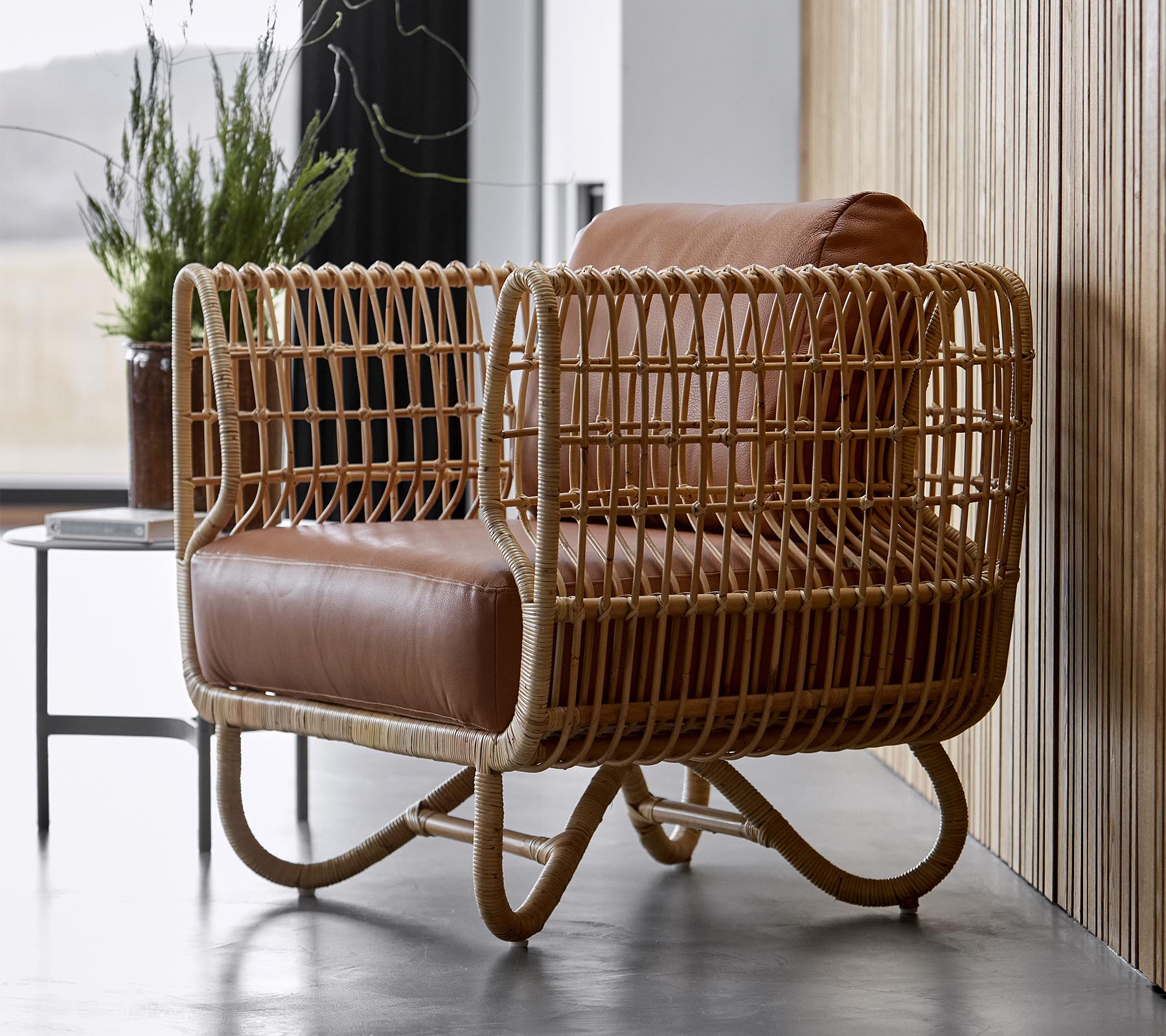 Sillón elegante con un marco de ratán tejido y cojines de cuero marrón suave, perfecto para una decoración moderna.