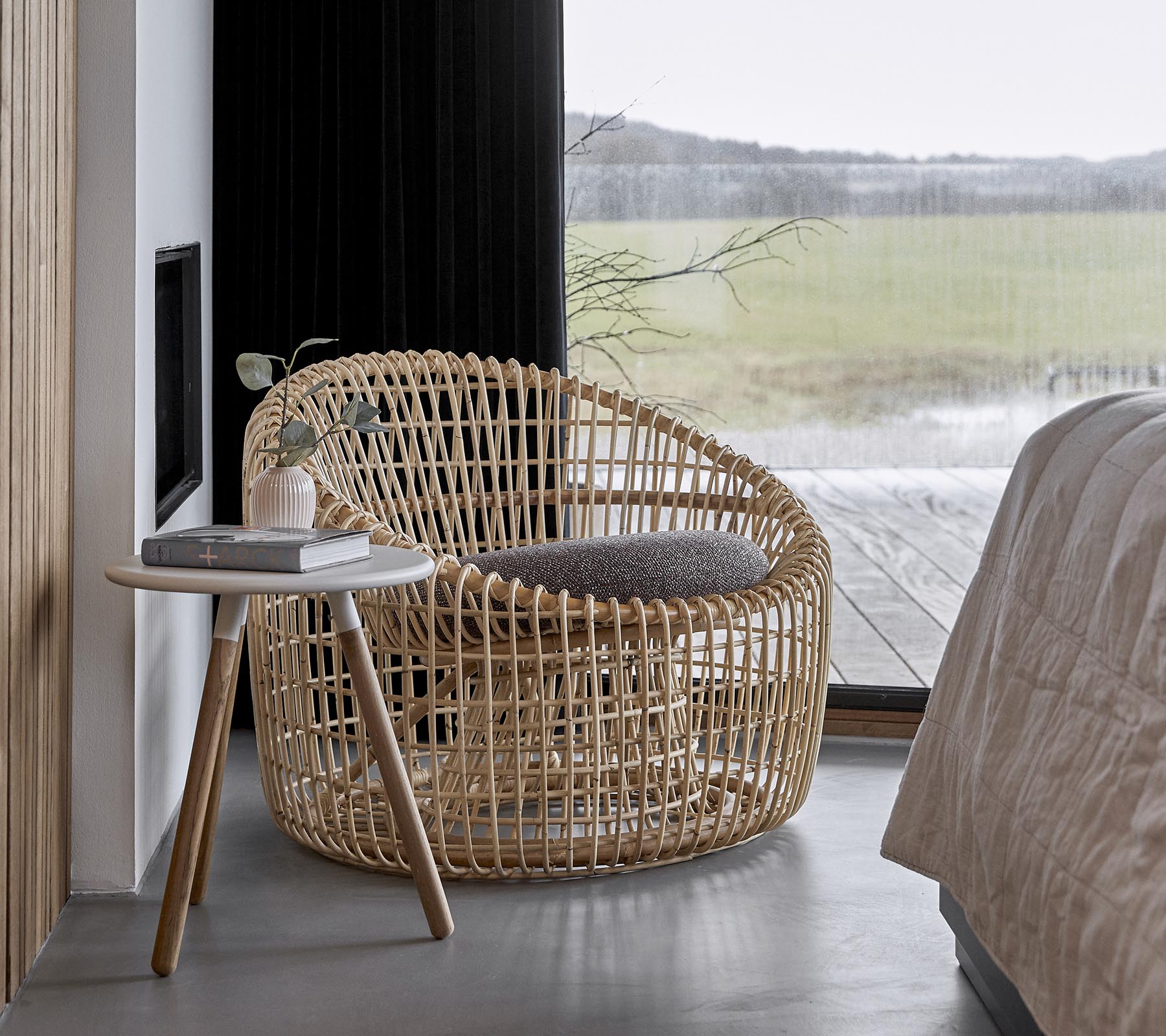 Una silla tejida con estilo acompañada de una pequeña mesa lateral, ubicada en un entorno sereno con grandes ventanas que dejan entrar la luz natural.