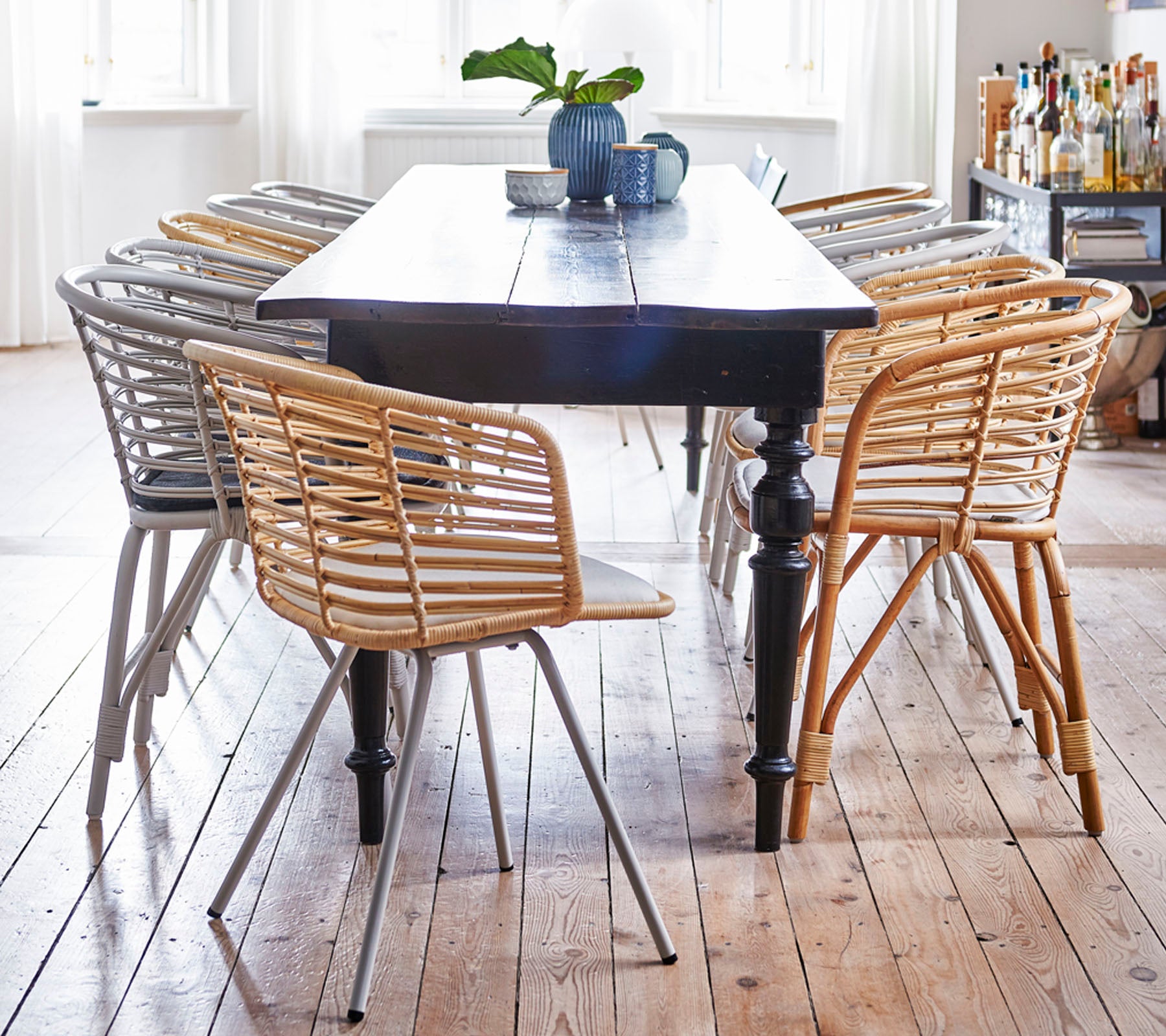 Una mesa de madera rodeada de sillas tejidas con estilo en tonos claros y oscuros, con una pequeña planta y una taza encima.