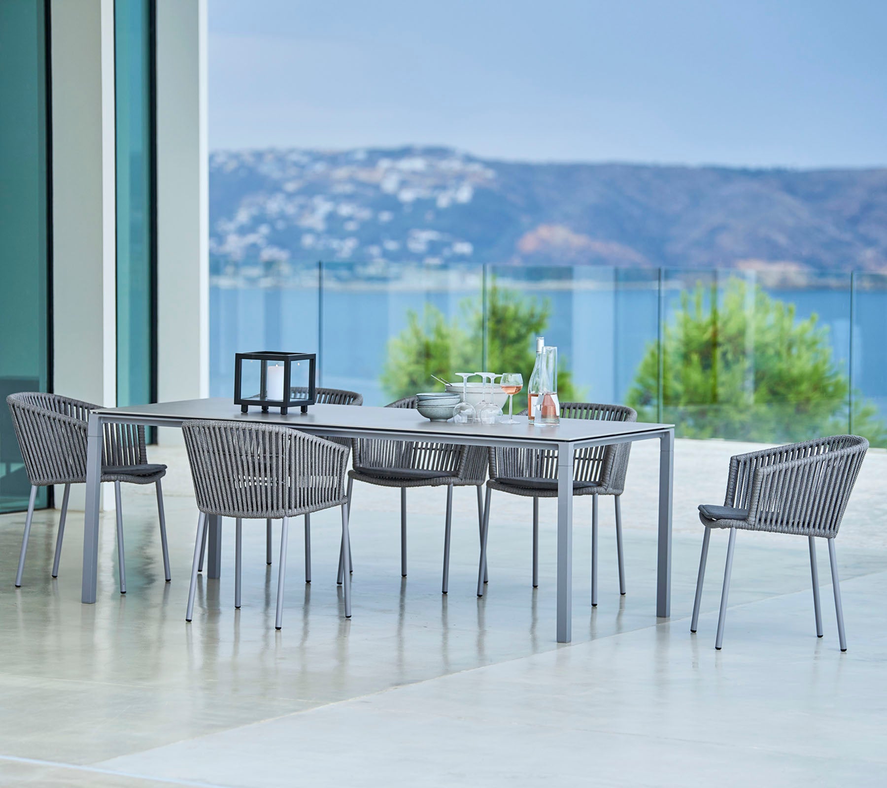 Elegante conjunto de comedor al aire libre con una mesa rectangular y sillas tejidas elegantes con vistas escénicas de fondo.