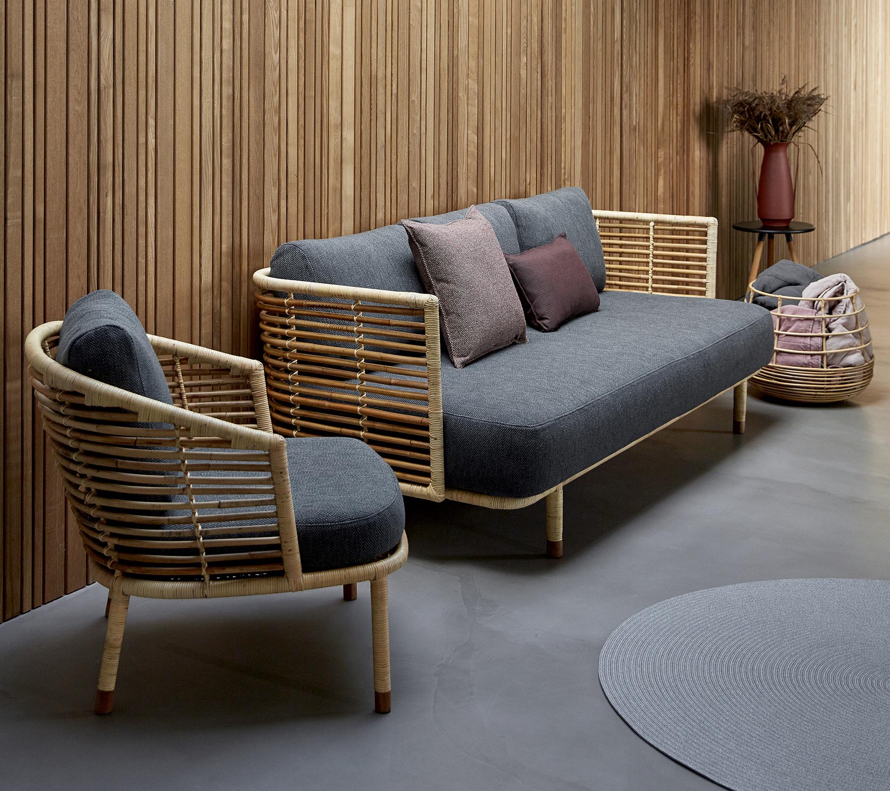 Disposición de asientos elegante con un sofá tapizado en gris con acentos de madera y una silla a juego, complementado con cojines decorativos.