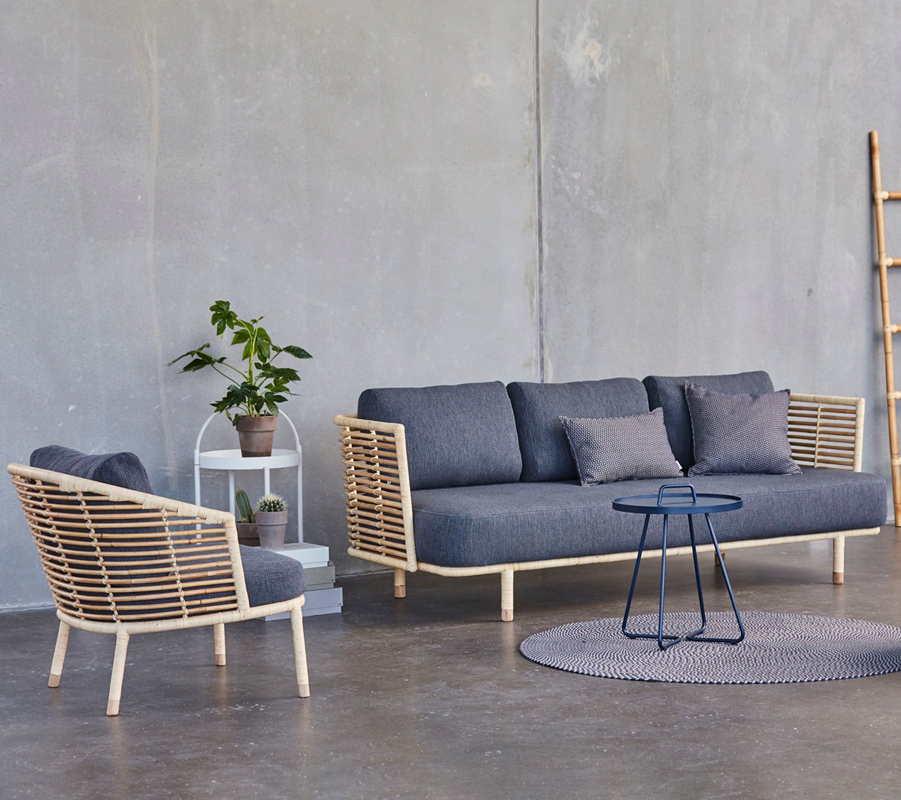 Un arreglo de asiento moderno que presenta un sofá y una silla elegante con acentos de madera, acompañado de una mesa auxiliar pequeña y una planta en maceta.