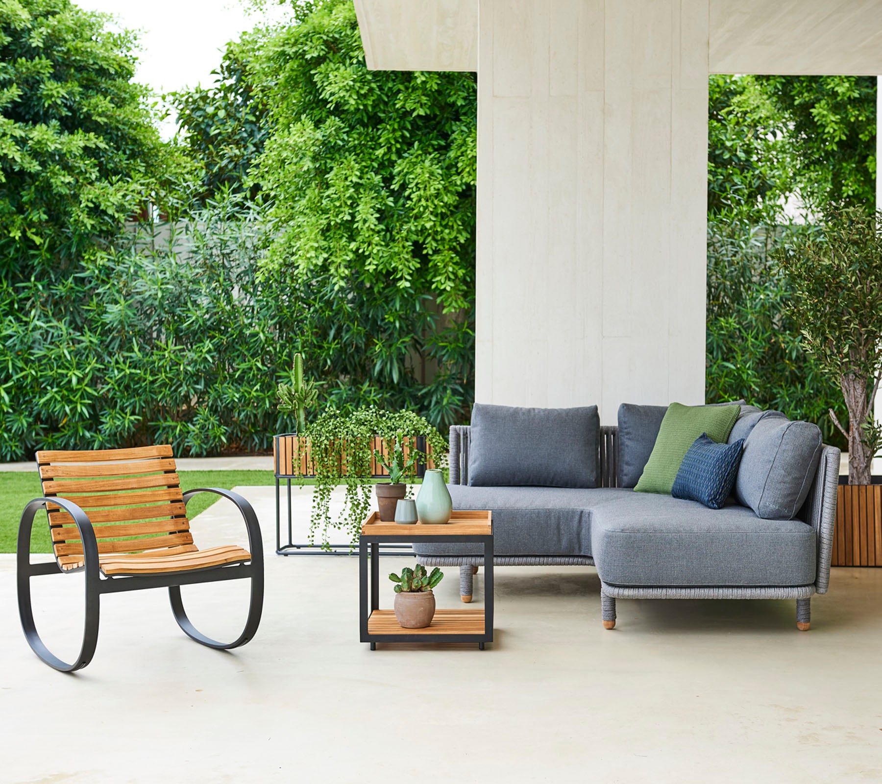 Disposición contemporánea de asientos con un sofá modular con cojines, una silla elegante y una mesa auxiliar con plantas decorativas.