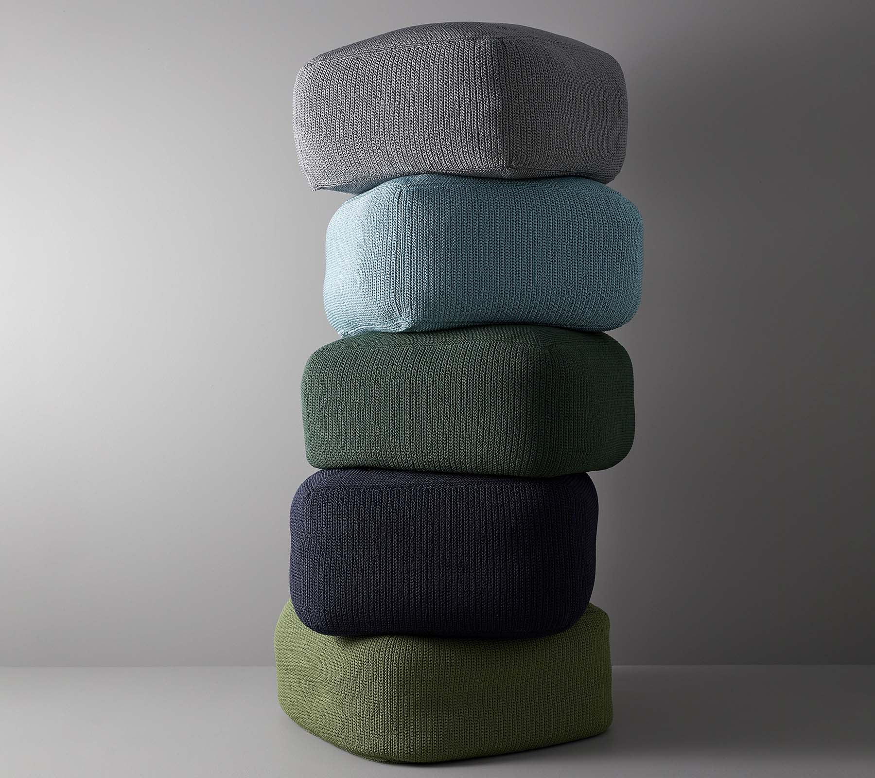 Una disposición apilada de cinco cojines en varios colores, incluyendo gris, azul claro, verde, azul oscuro y verde oliva.
