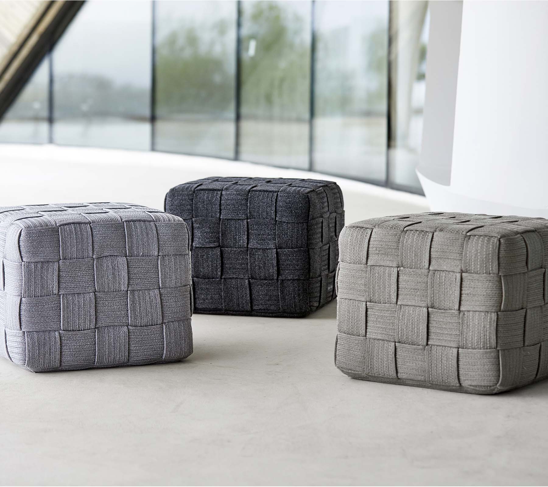 Tres poufs tejidos en diferentes tonos de gris, con un diseño texturizado, dispuestos sobre una superficie clara. Ideales para sentarse o decorar.