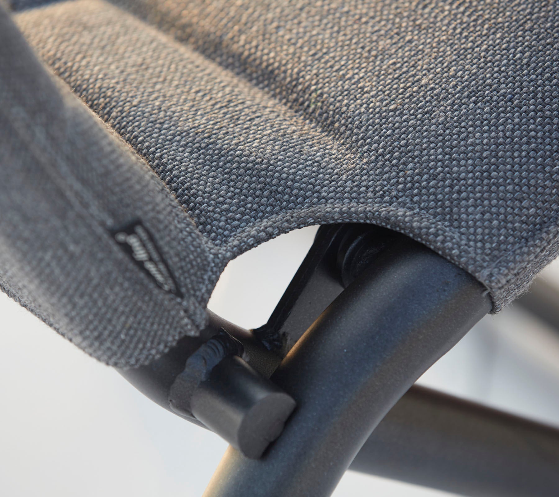 Primer plano del asiento de tela texturizada de una silla y su robusto marco negro, destacando las costuras y los detalles de diseño.