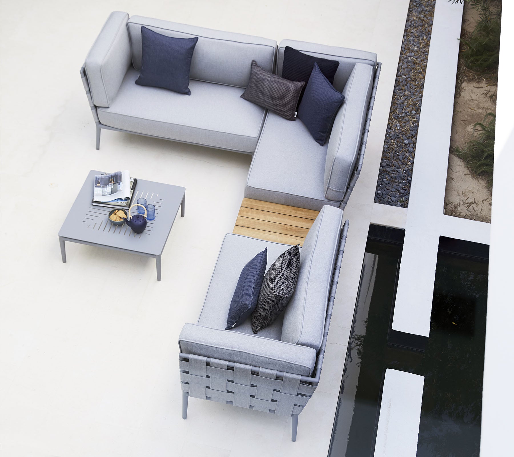 Conjunto de asientos al aire libre moderno con cojines grises, acentuado por cojines oscuros, complementado por una mesa minimalista.