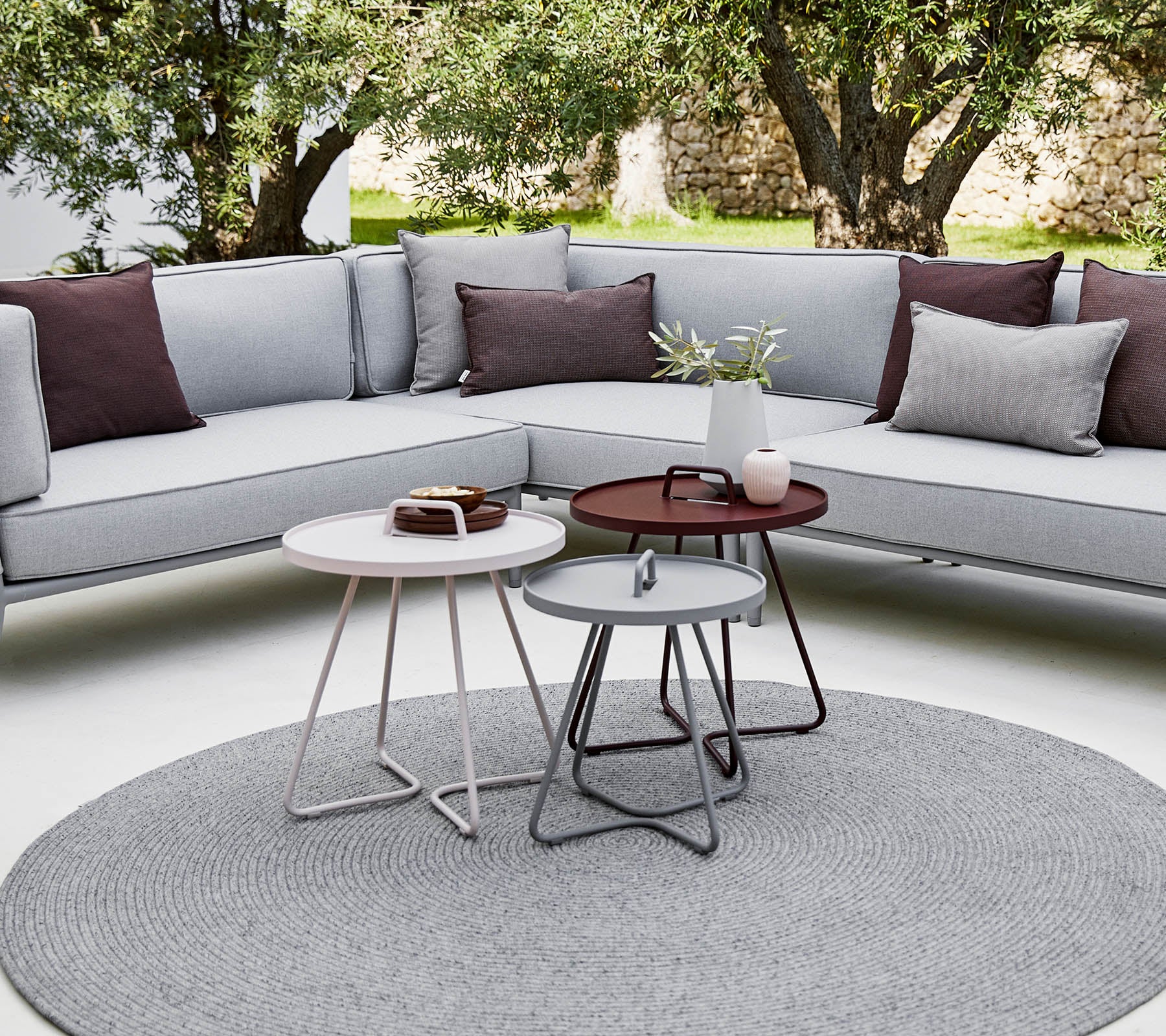 Área de estar al aire libre con estilo, que cuenta con un sofá seccional con cojines y mesas de café redondas modernas en un ambiente relajado y contemporáneo.