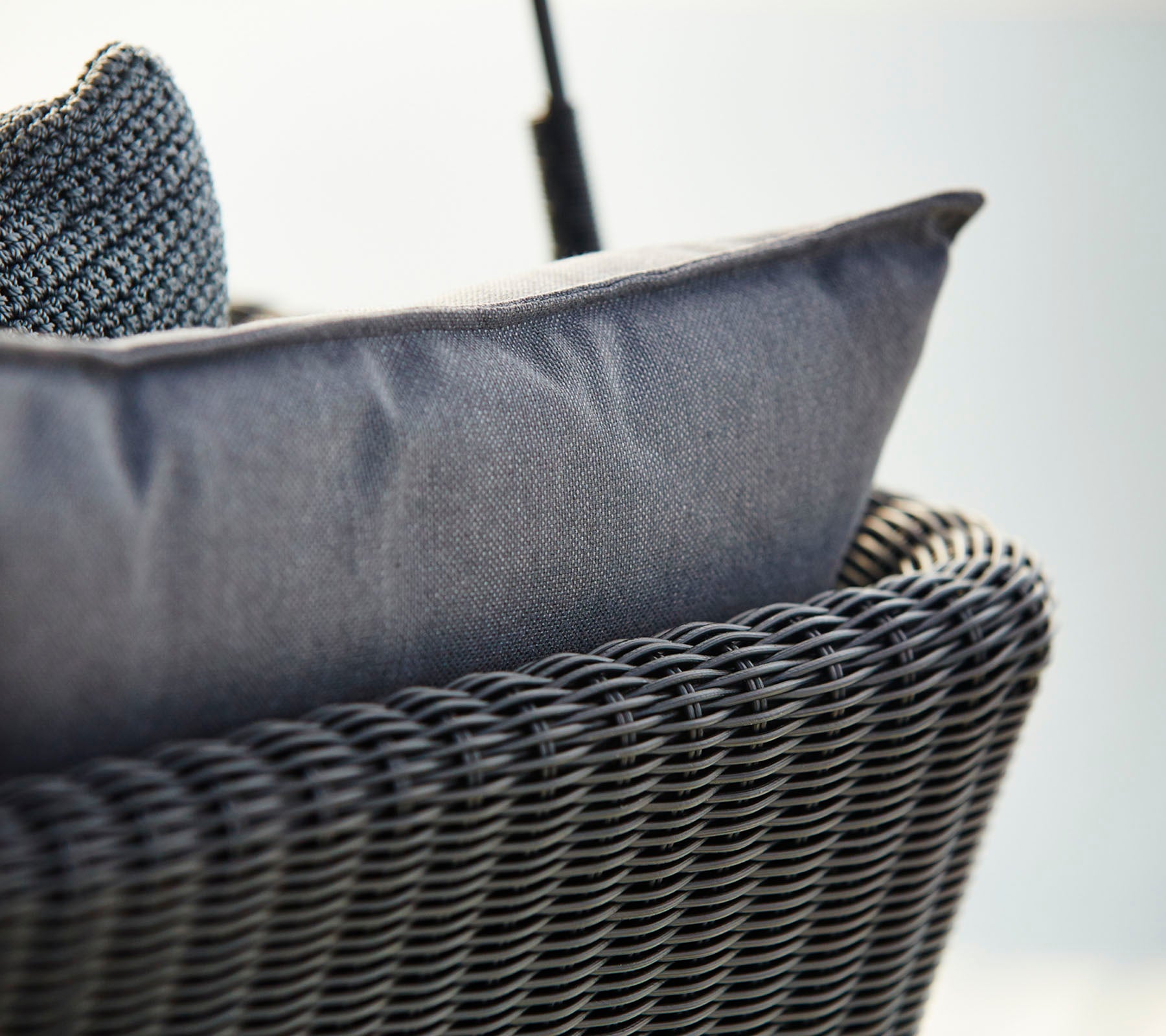 Primer plano de una silla de estilo cesta tejida con un cojín texturizado de color gris oscuro, enfatizando la comodidad y el diseño moderno.