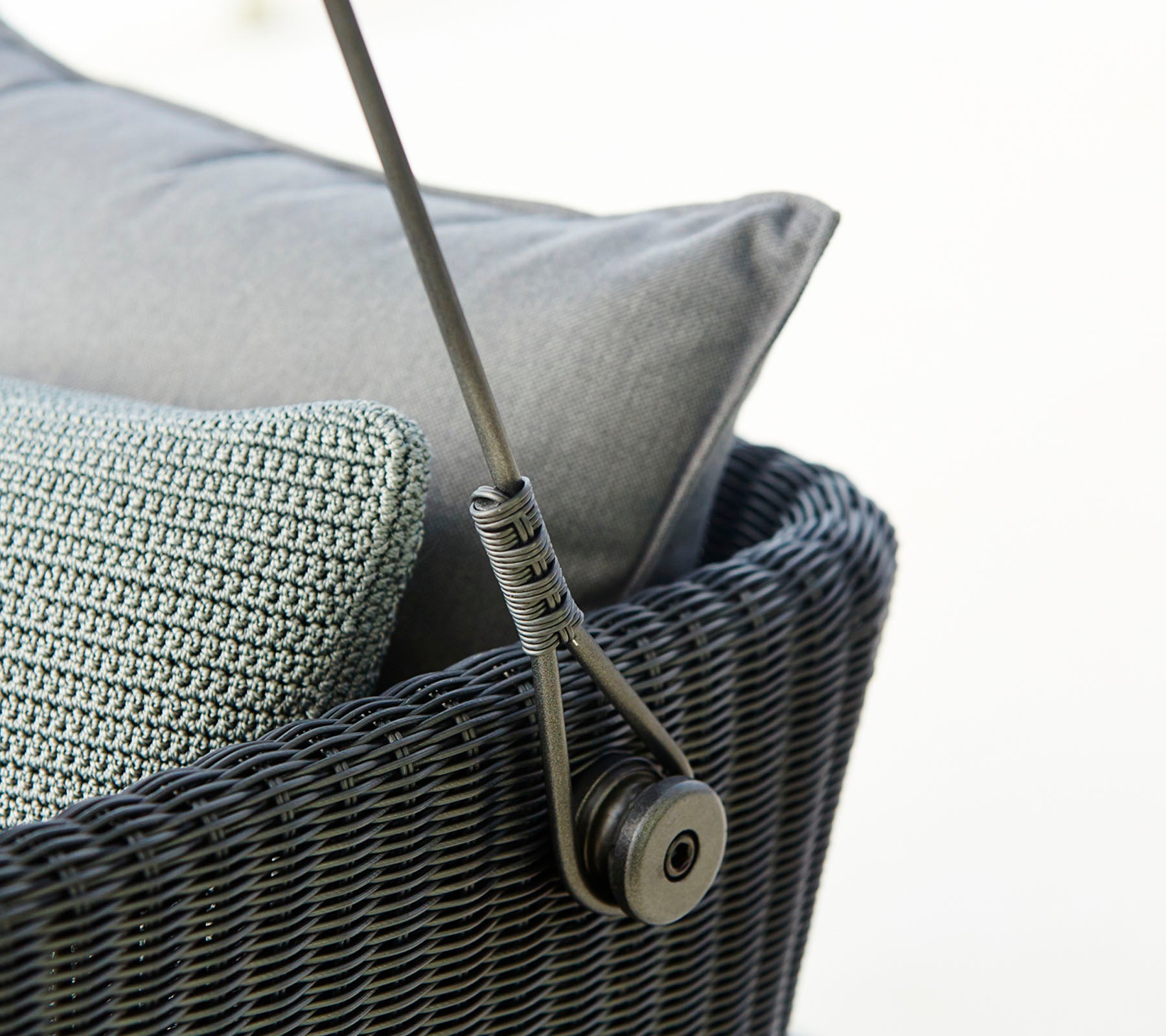 Primer plano de una elegante pieza de asiento tejida con cojines grises y un mecanismo de soporte elegante. Ideal para una decoración moderna.