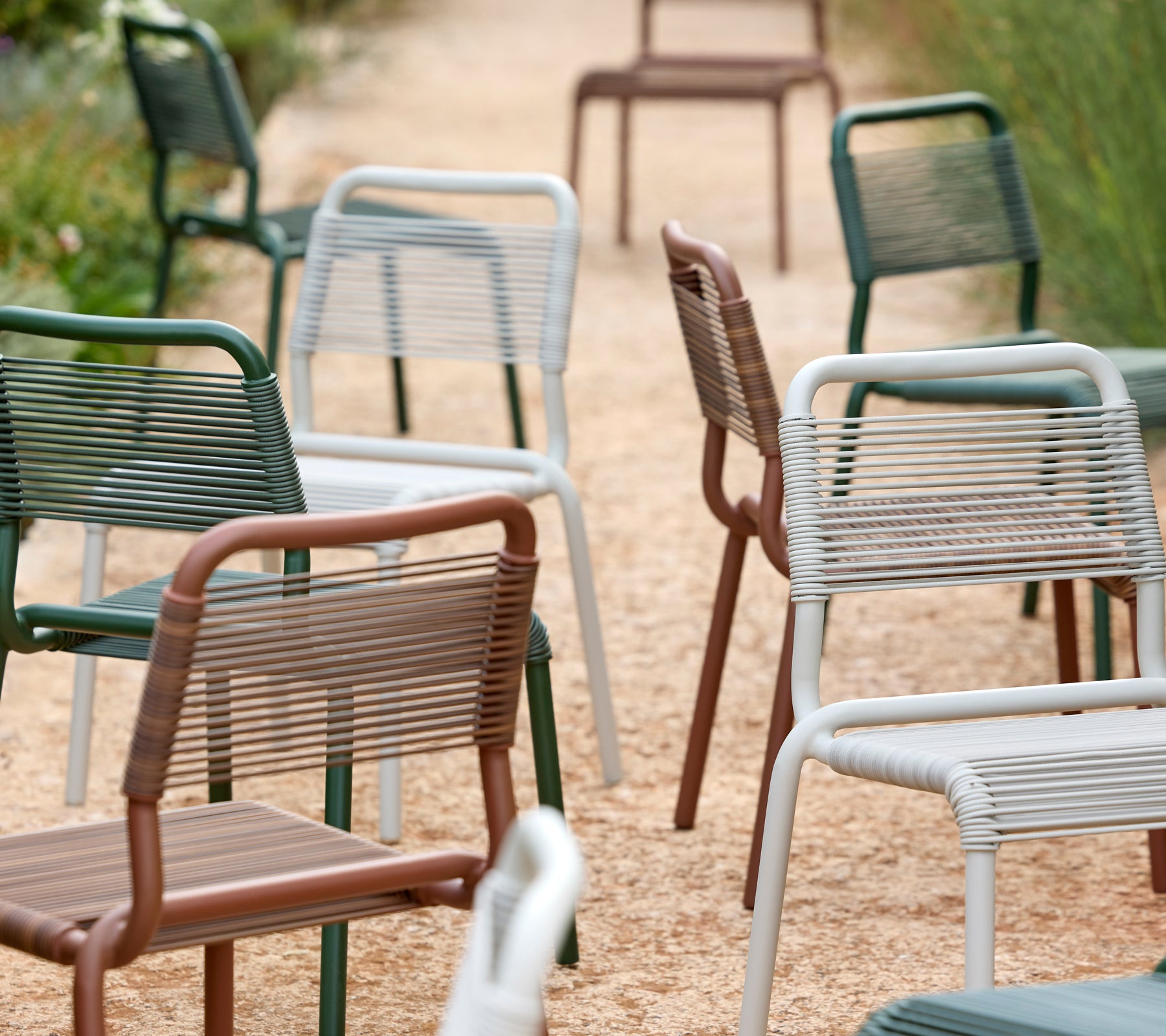 Una fila de sillas modernas en verde, gris, marrón y blanco en un camino de grava.