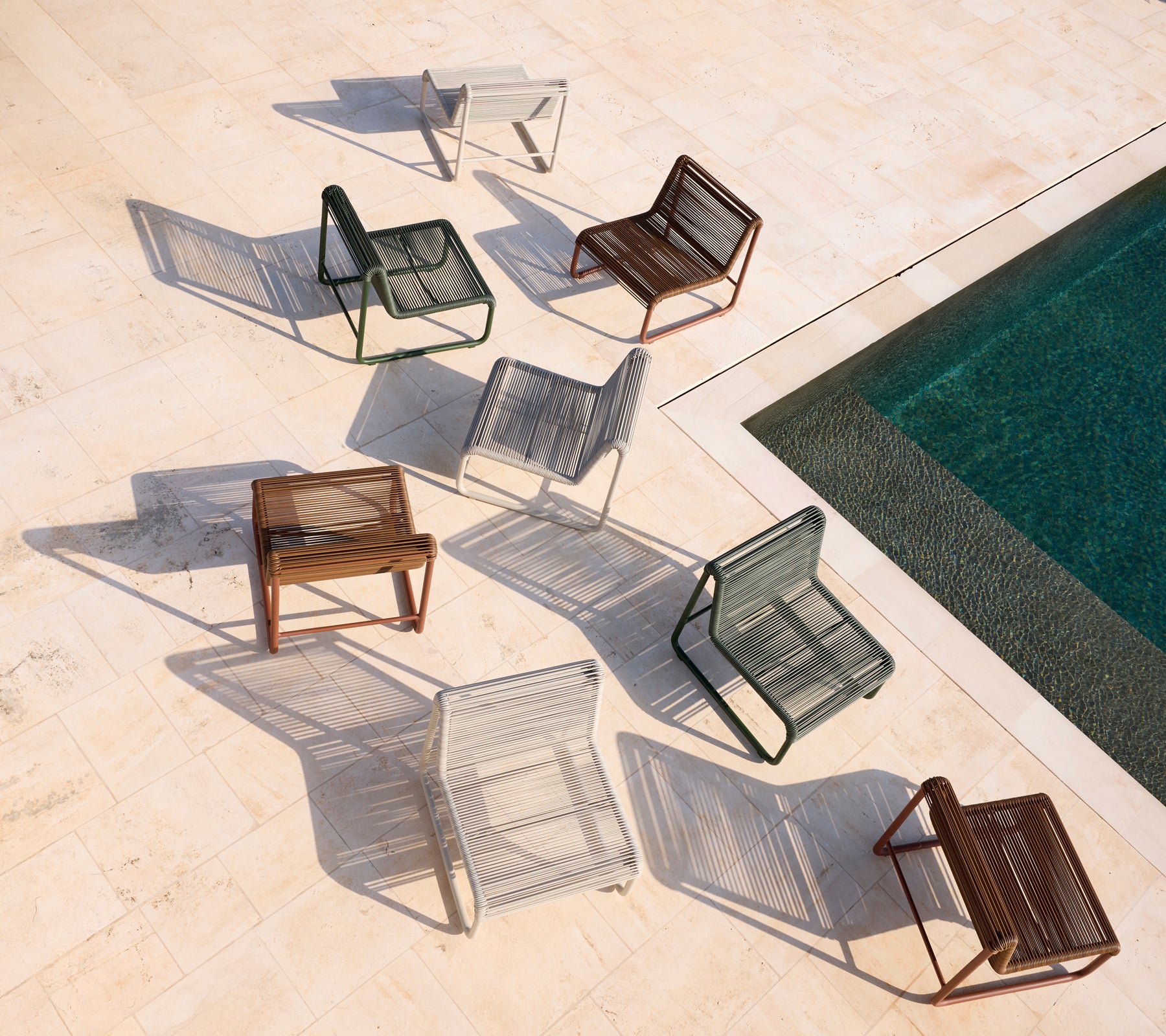 Sillas modernas variadas en marrón, gris, blanco y negro dispuestas alrededor de una piscina.