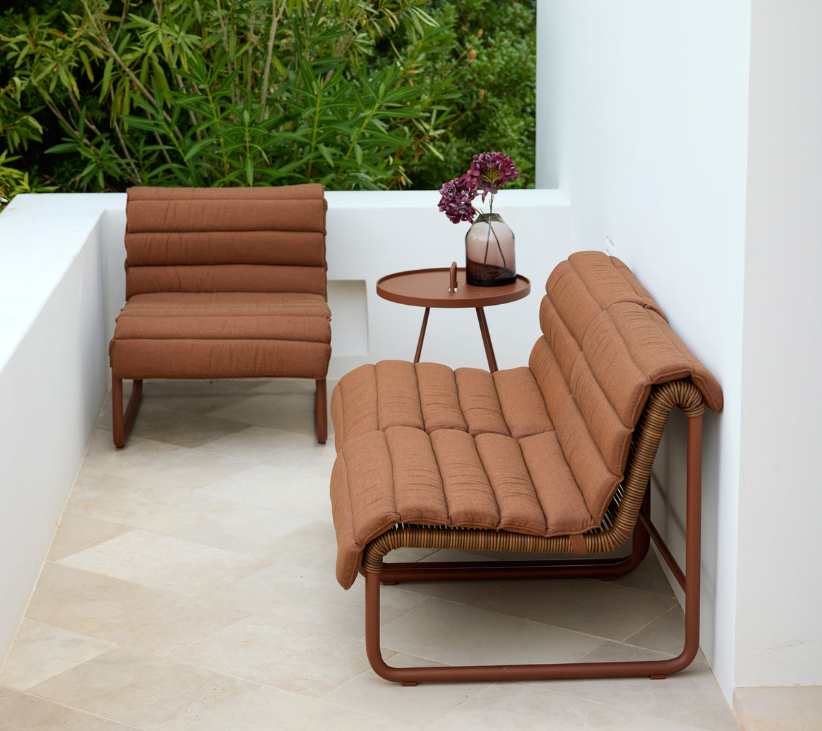 Sillón y loveseat marrón con una mesa auxiliar redonda en un entorno exterior moderno.