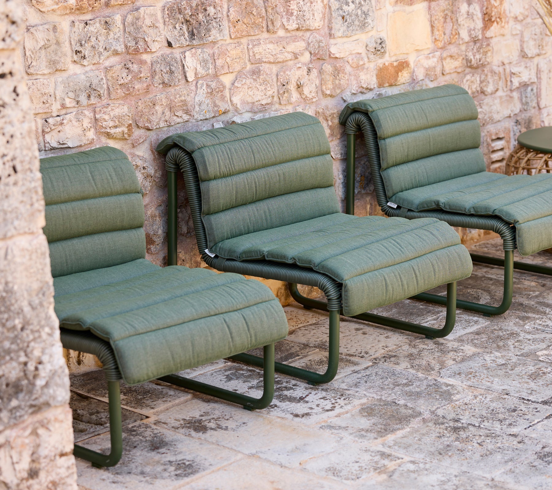 Sillas de lounge verdes dispuestas contra una pared de piedra.