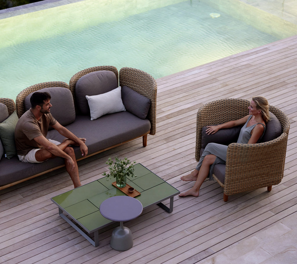 Dos personas sentadas en cómodas sillas de salón alrededor de una mesa de café elegante, con una serena fuente de agua en el fondo.