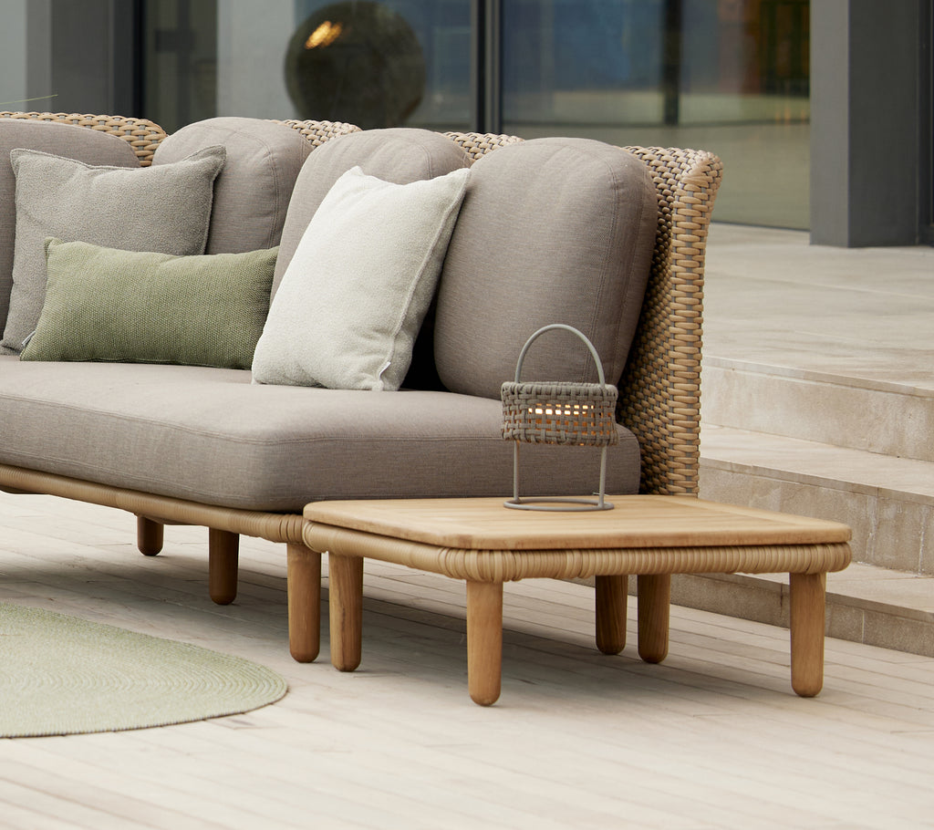 Mesa de café con arco elegante con una parte superior de teca, junto a cojines en un sofá moderno, complementada por una lámpara decorativa Illusion.