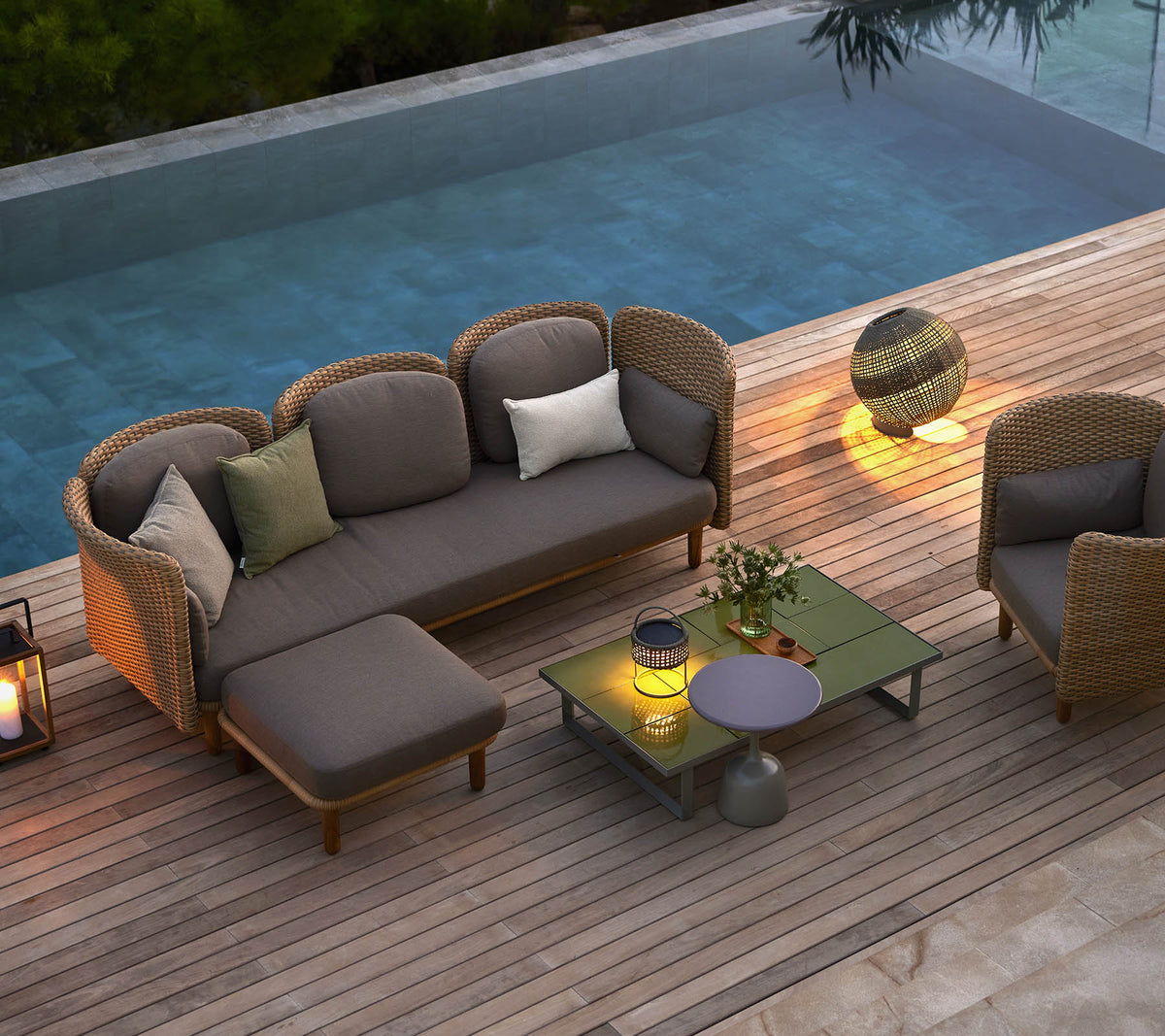 Asientos de lounge elegantes con cojines, una mesa de café y iluminación ambiental, colocados junto a una piscina serena.