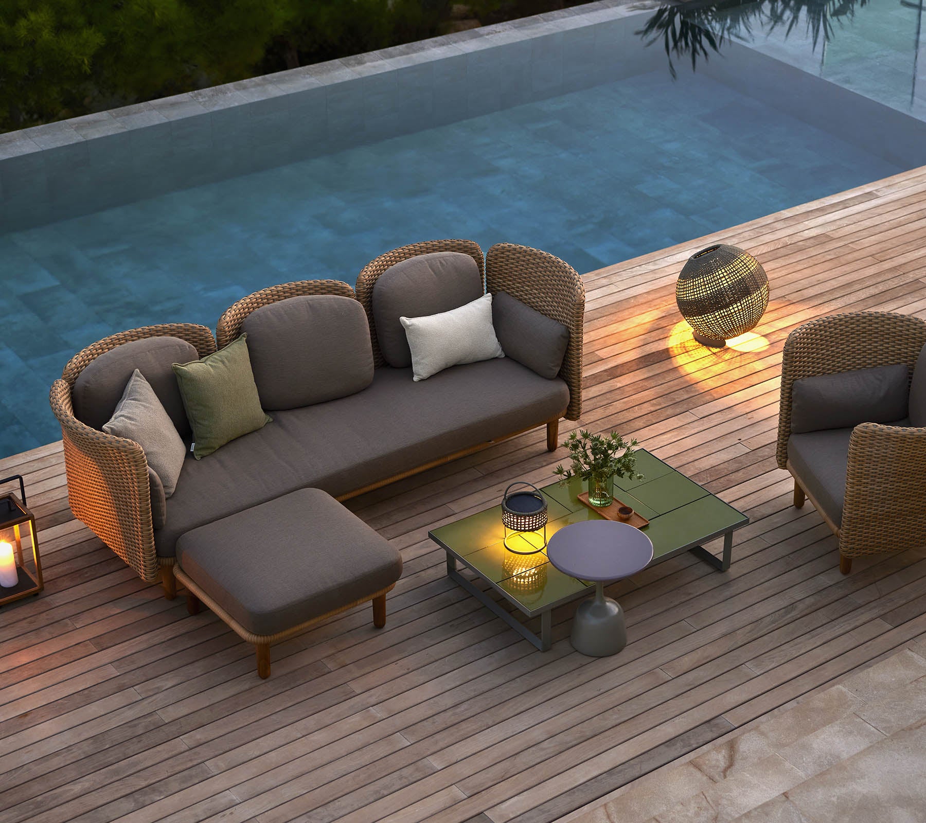 Asientos de lounge elegantes con cojines, una mesa de café y iluminación ambiental, colocados junto a una piscina serena.