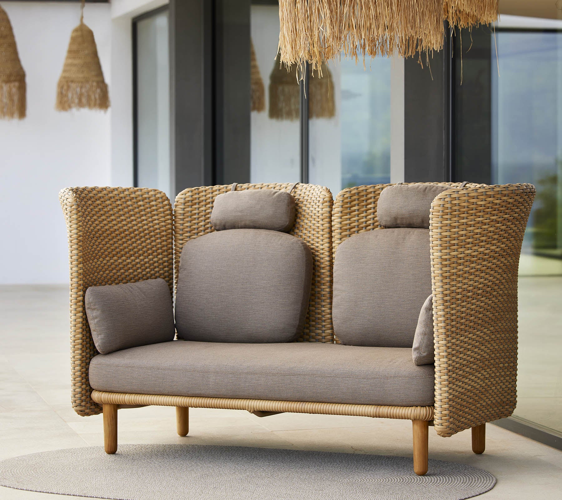 Un sofá lounge elegante con laterales trenzados y almohadas suaves, diseñado para la comodidad y la relajación. Ideal para espacios modernos.