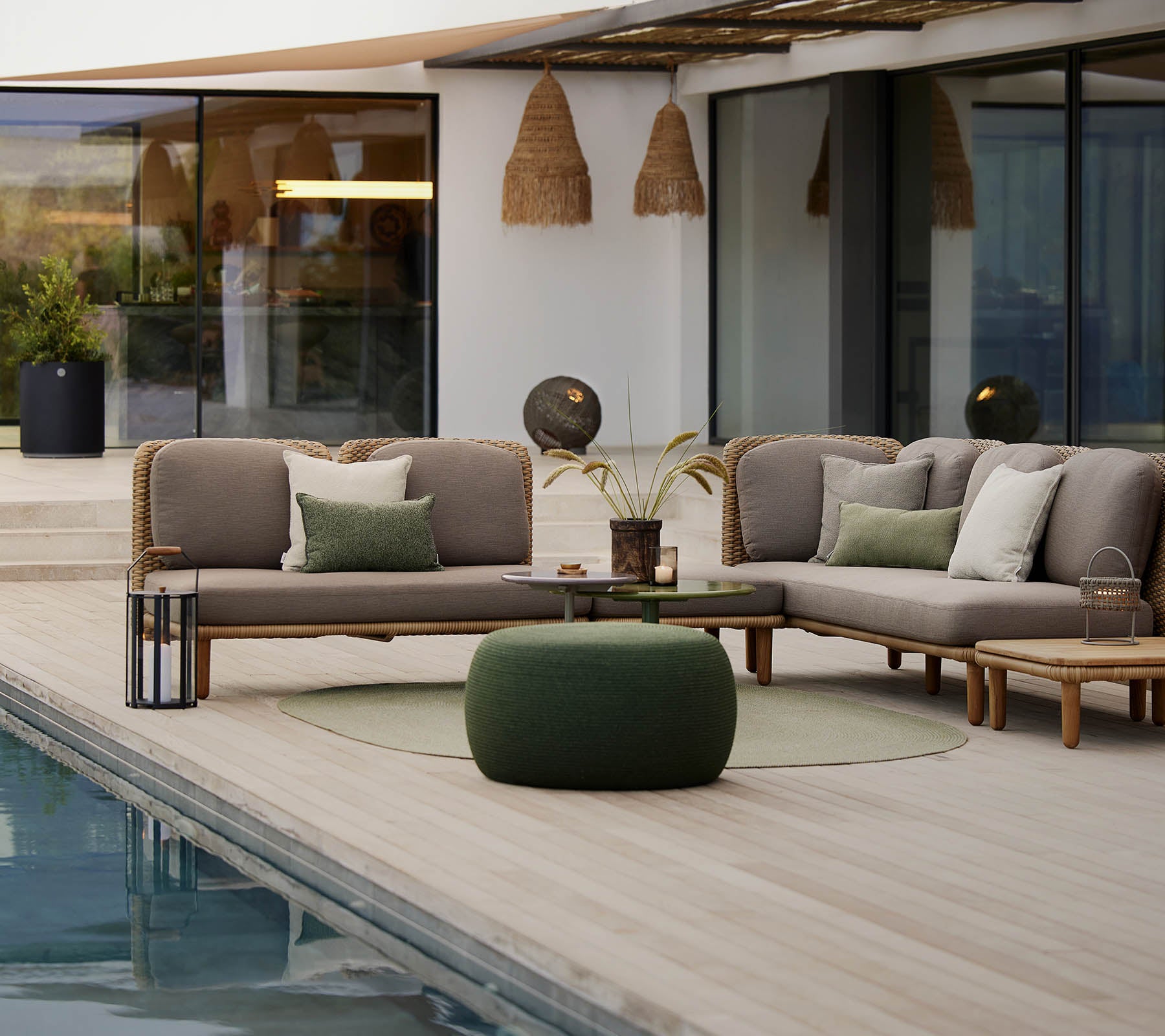 Una elegante zona de lounge con un sofá seccional con cojines, una mesa redonda y un puff acogedor, ubicado junto a una tranquila piscina.