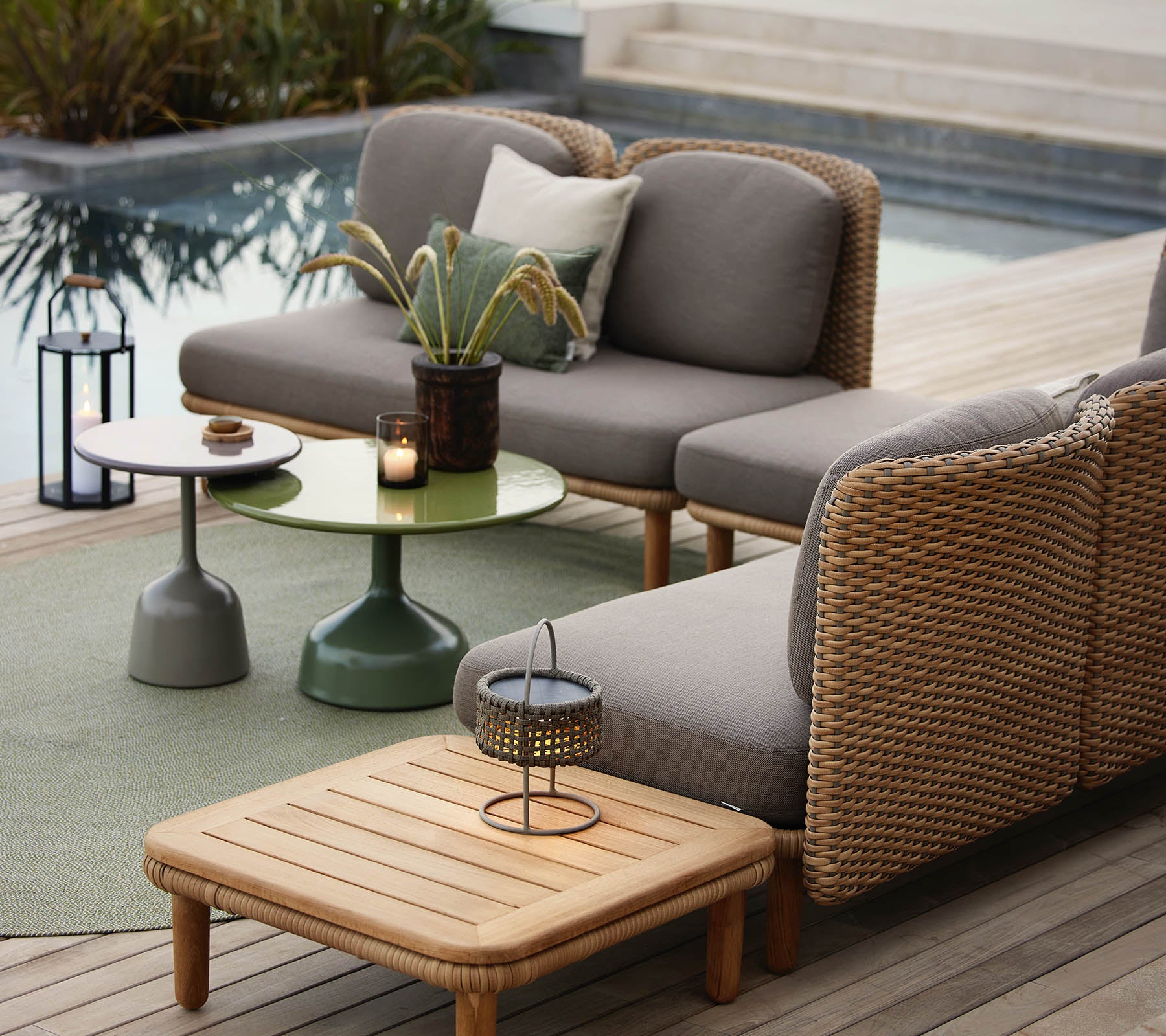 Una zona de lounge elegante con un sofá gris con acentos de mimbre, una mesita verde y accesorios decorativos.