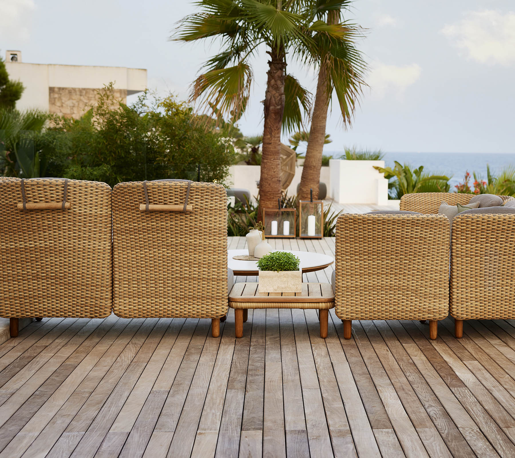 Una fila de sillones tejidos que dan a una vista escénica, con una terraza de madera y plantas tropicales al fondo.
