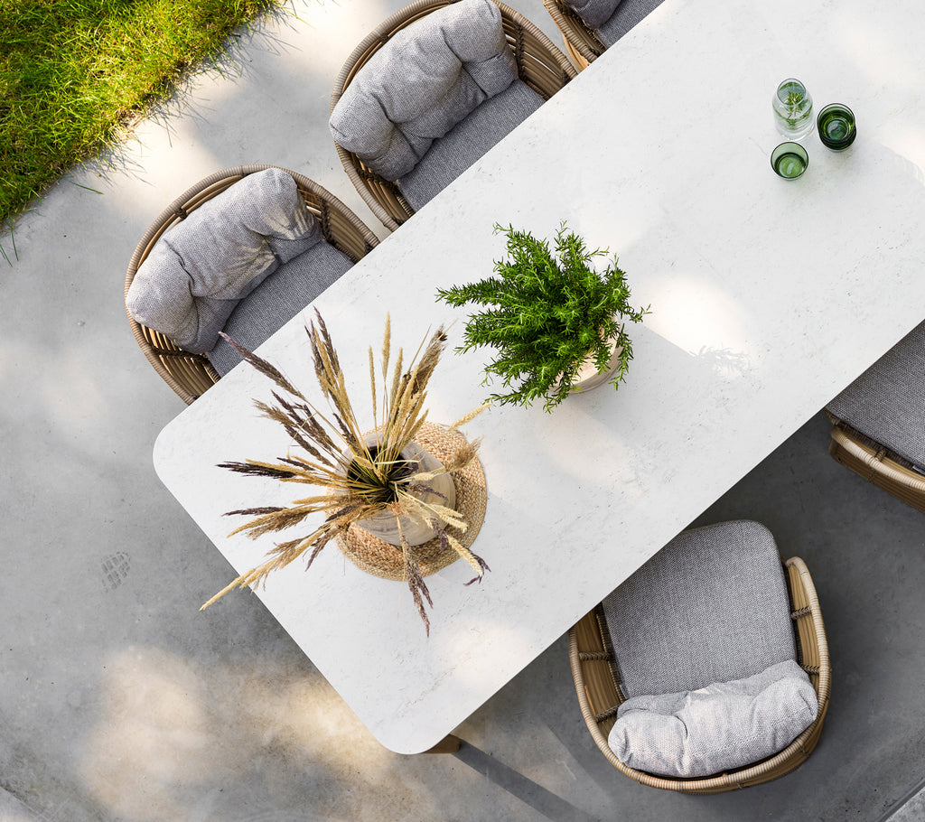 Una mesa de comedor moderna con una superficie texturizada, rodeada de sillas acolchadas y adornada con un elegante centro de plantas.