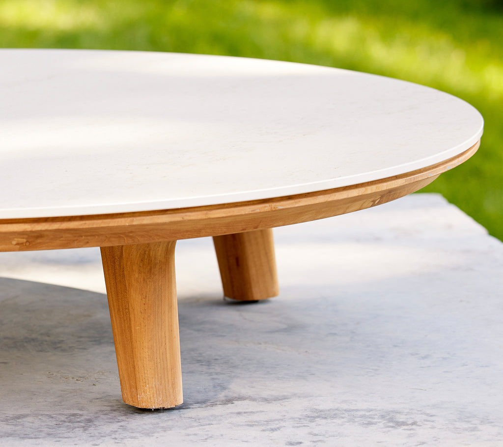 Acercamiento a una mesa de café circular con una superficie suave y patas de madera, destacando su diseño elegante y su artesanía.