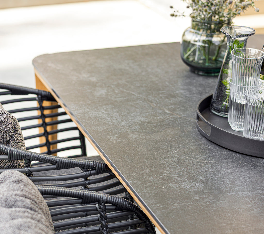 Una configuración moderna de comedor con una mesa suave, una silla de mimbre elegante, cristalería en una bandeja y un jarrón decorativo con vegetación.
