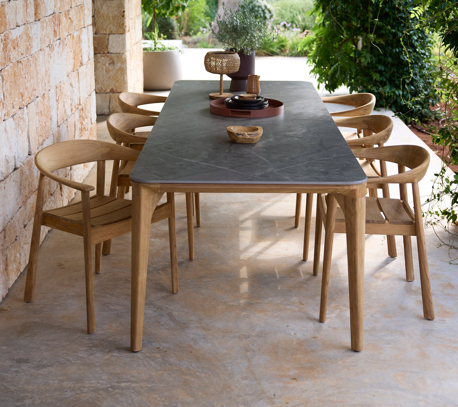 Mesa de comedor moderna para exteriores con superficie negra y sillas de madera en un entorno natural.